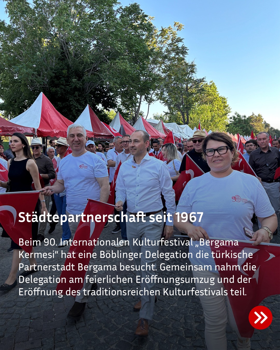 Eine Gruppe von Personen marschiert bei einem Festumzug, wobei drei im Vordergrund türkische Flaggen halten. Im Hintergrund stehen rote und weiße Zelte unter Bäumen. Ein Textfeld mit der Überschrift „Städtepartnerschaft seit 1967“ beschreibt den Besuch einer Böblinger Delegation beim 90. Internationalen Kulturfestival „Bergama Kermesi“ in der Partnerstadt Bergama. (KI-Alternativtext)