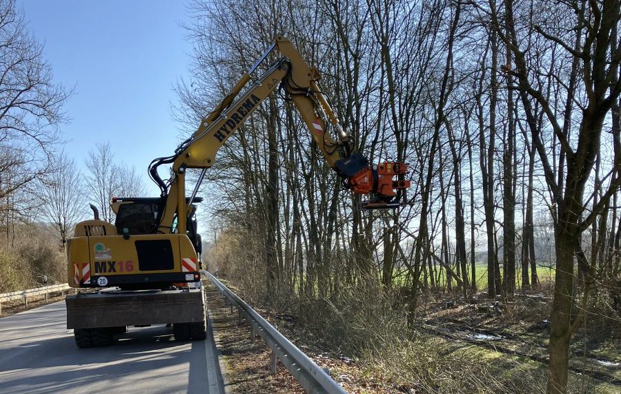Gehölzbagger im Einsatz an einer Straße. 