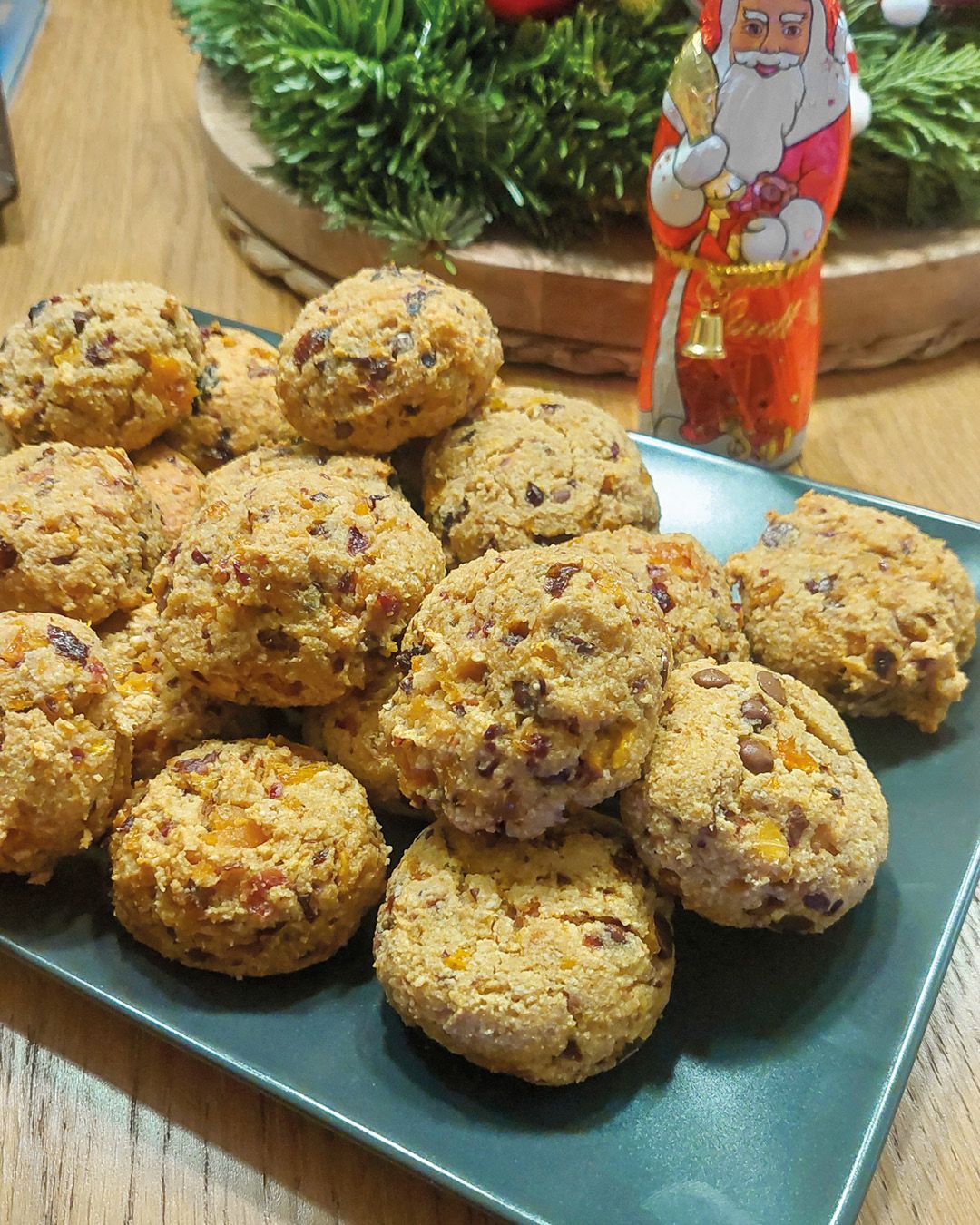 Dieser Alternativtext wurde KI-generiert: Ein Teller mit einigen runden Keksen steht im Vordergrund. Im Hintergrund ist weihnachtliche Dekoration zu sehen.