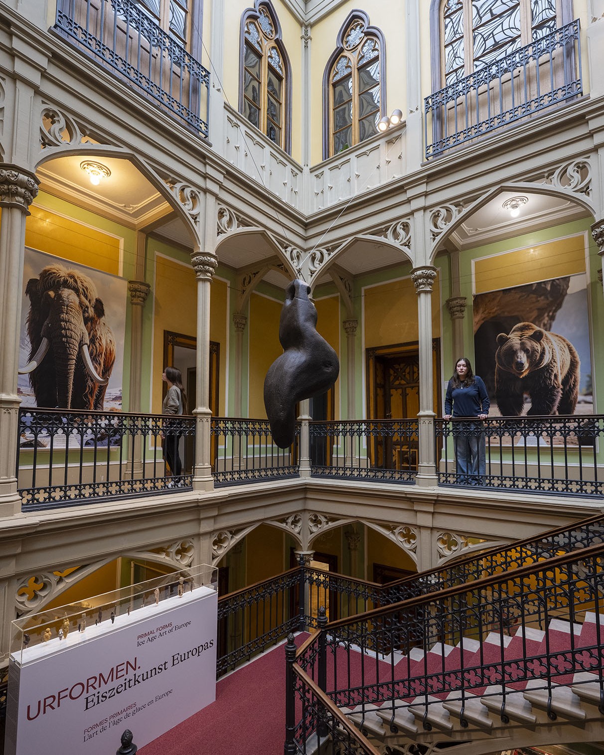 Dieser Alternativtext wurde KI-generiert: Innenansicht eines Museumsgebäudes mit Galerien und einer Treppe. Große Bilder von Tieren und eine abstrakte Skulptur sind zu sehen.