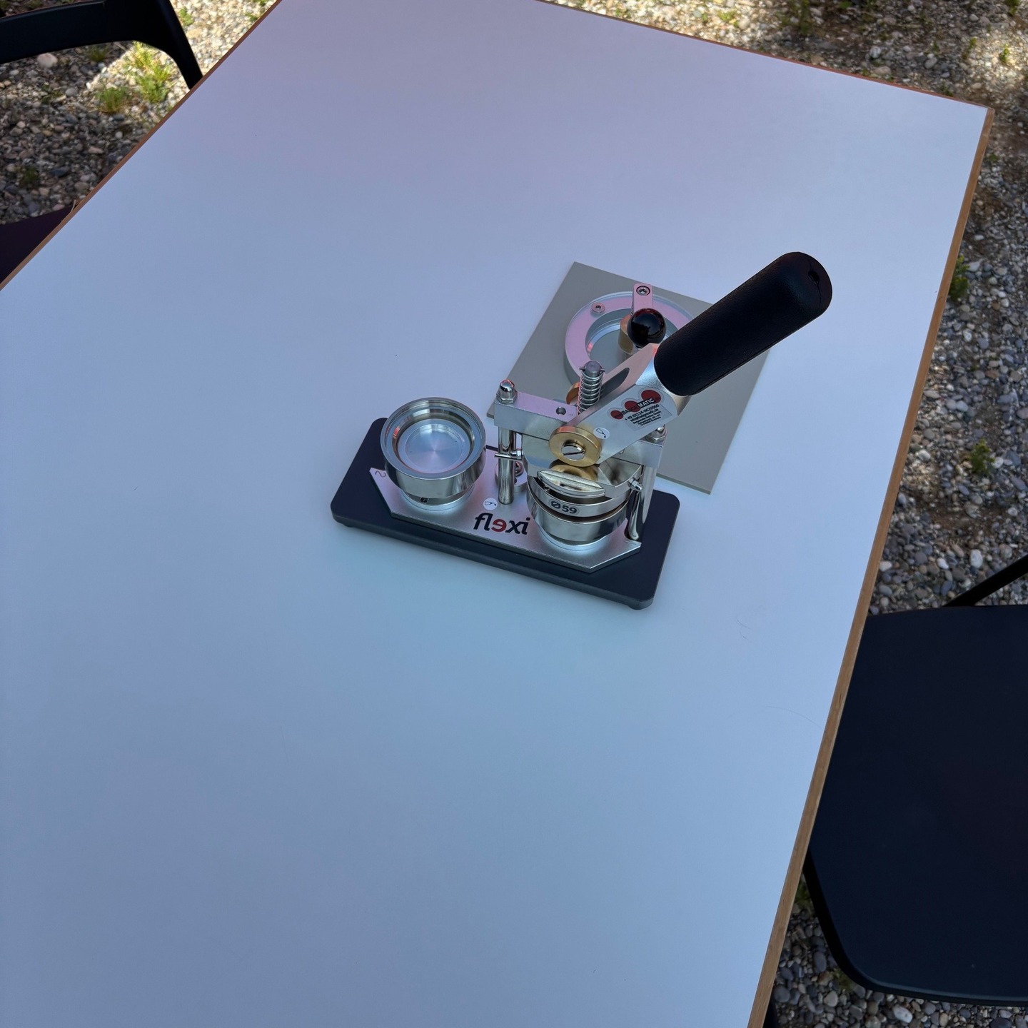 Close-up of a white table with a badge-making machine. The device is predominantly silver with black accents.