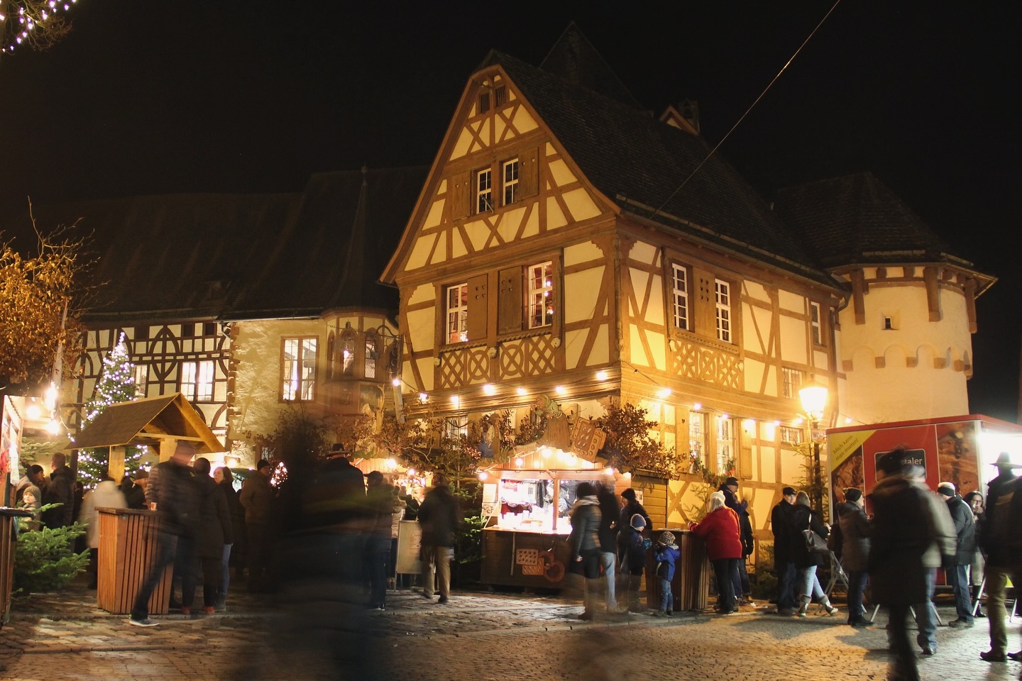 Ein beleuchteter Weihnachtsmarkt an einem Abend vor Fachwerkhäusern. Viele Menschen bummeln über den Markt.