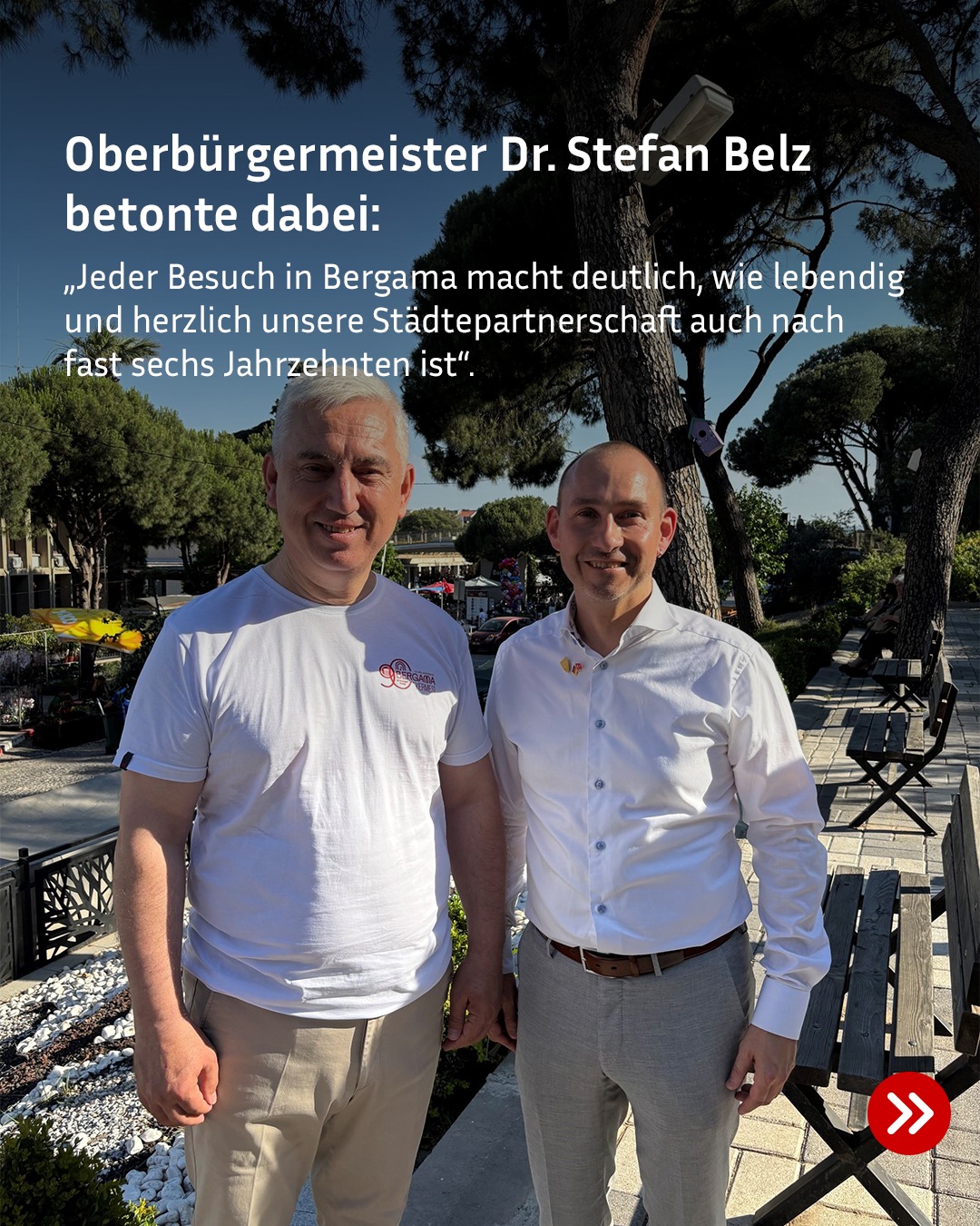 Zwei Personen stehen im Freien nebeneinander und lächeln. Die Person links trägt ein T-Shirt mit dem Logo „Bergama“. Der Text im Bild lautet: „Oberbürgermeister Dr. Stefan Belz betonte dabei: ‚Jeder Besuch in Bergama macht deutlich, wie lebendig und herzlich unsere Städtepartnerschaft auch nach fast sechs Jahrzehnten ist‘.“ (KI-Alternativtext)