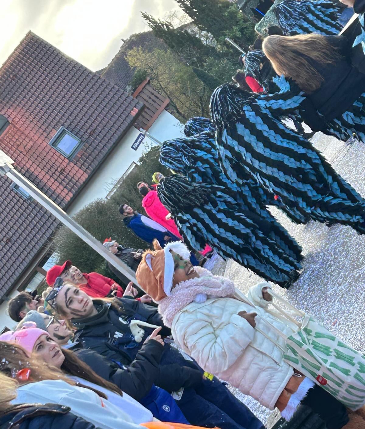 Dieser Alternativtext wurde KI-generiert: Ein farbiges Foto zeigt eine Gruppe von Personen im Freien. Einige tragen Kostüme, darunter ein großes, blaues Tierkostüm und ein weiteres in Form eines Tierkopfes.