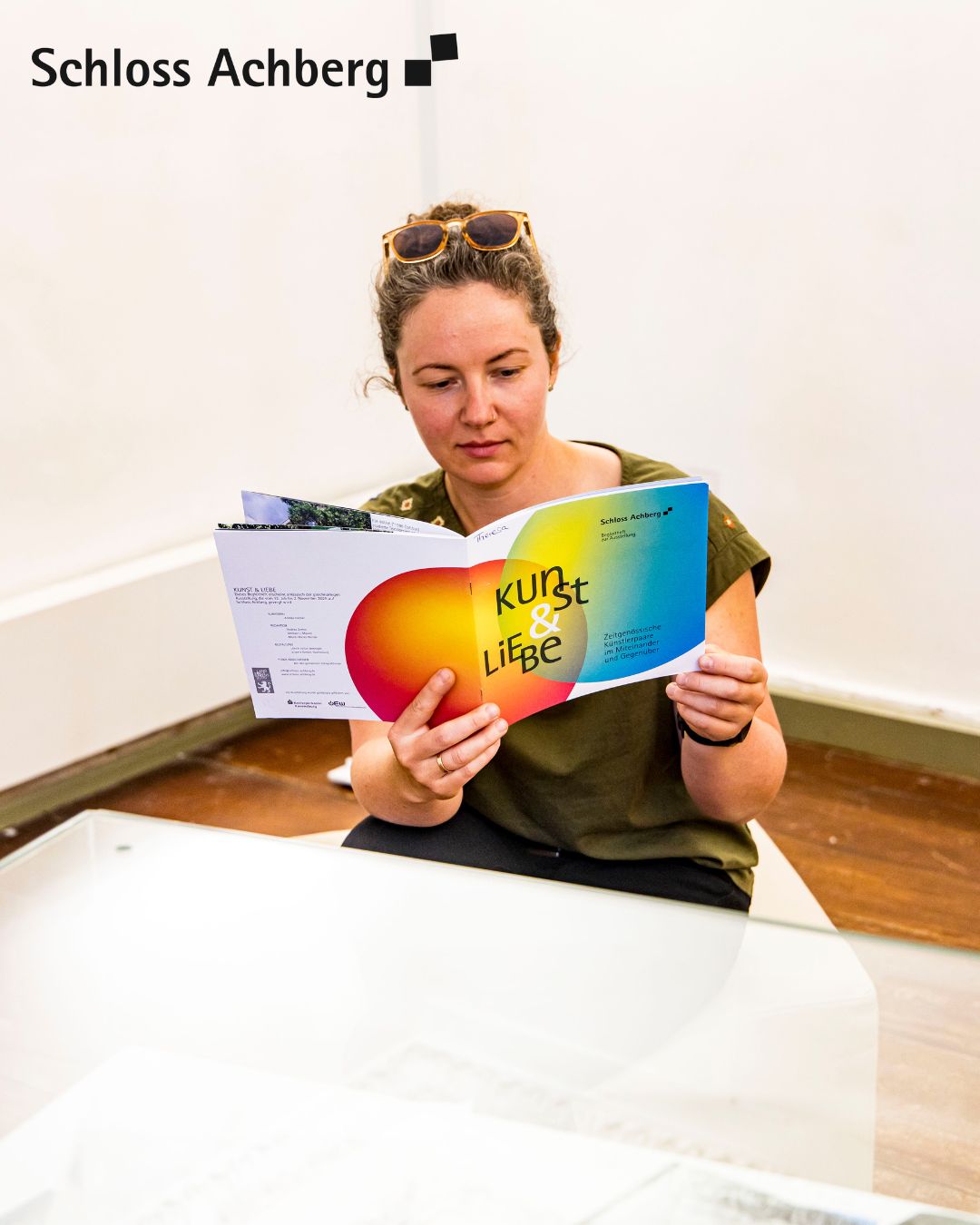 Eine Person sitzt an einem Tisch und liest eine Broschüre mit dem Titel "Kunst & Liebe".