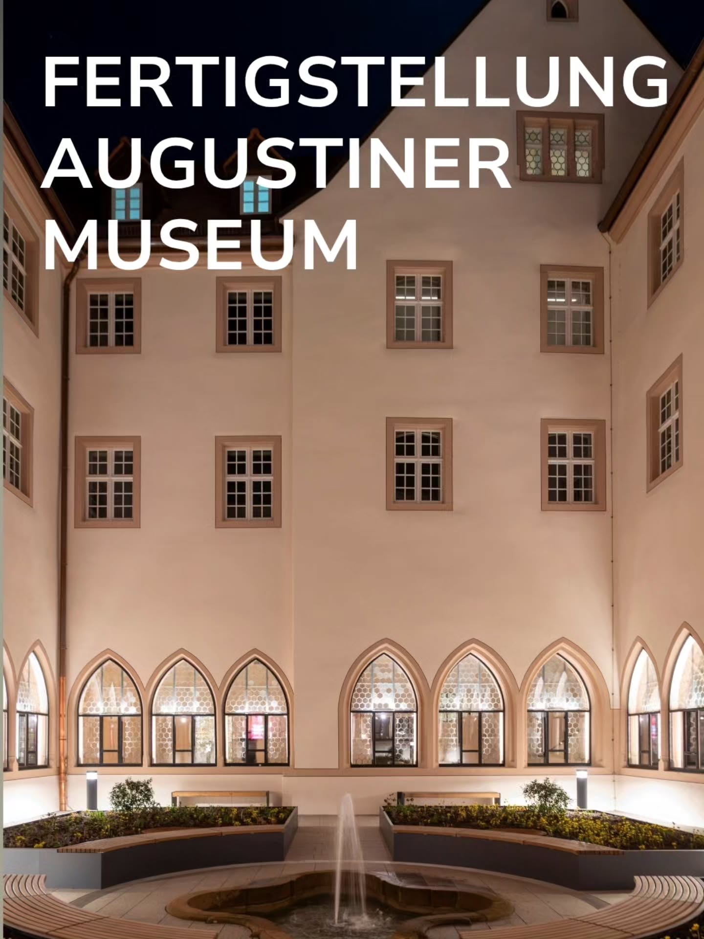 Großer weißer Text "FERTIGSTELLUNG AUGUSTINER MUSEUM" oben links. Im Hintergrund ein hell verputztes Gebäude mit rechteckigen Fenstern im Obergeschoss und spitzbogigen Fenstern im Erdgeschoss. Im Vordergrund ein Innenhof mit einer Springbrunnenanlage, Beeten und Bänken bei Nacht. (KI-Alternativtext)