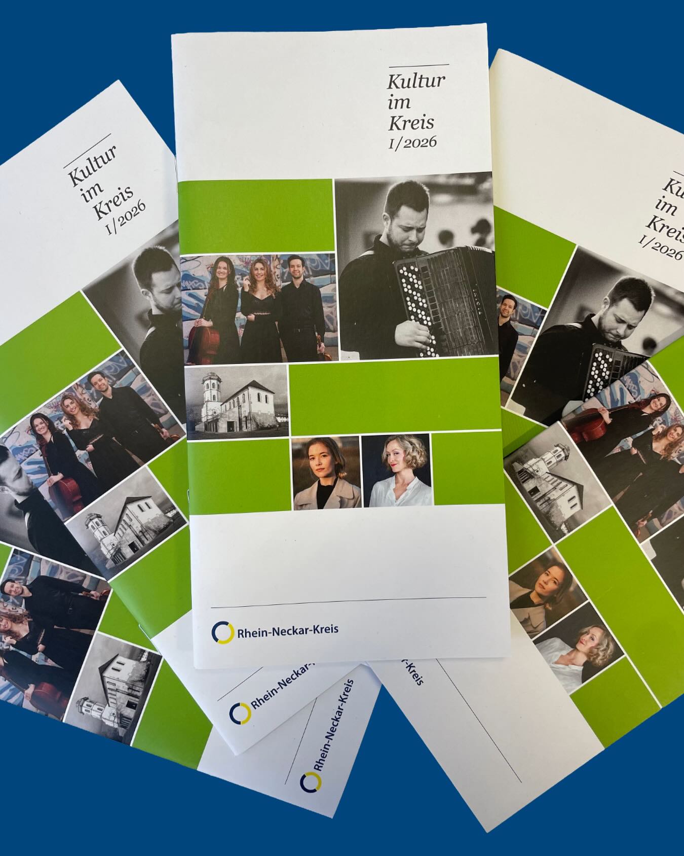 Dieser Alternativtext wurde KI-generiert: Mehrere Broschüren und Flyer liegen übereinander auf einem blauen Untergrund. Die Dokumente zeigen Porträts von Menschen und Bilder von Gebäuden.