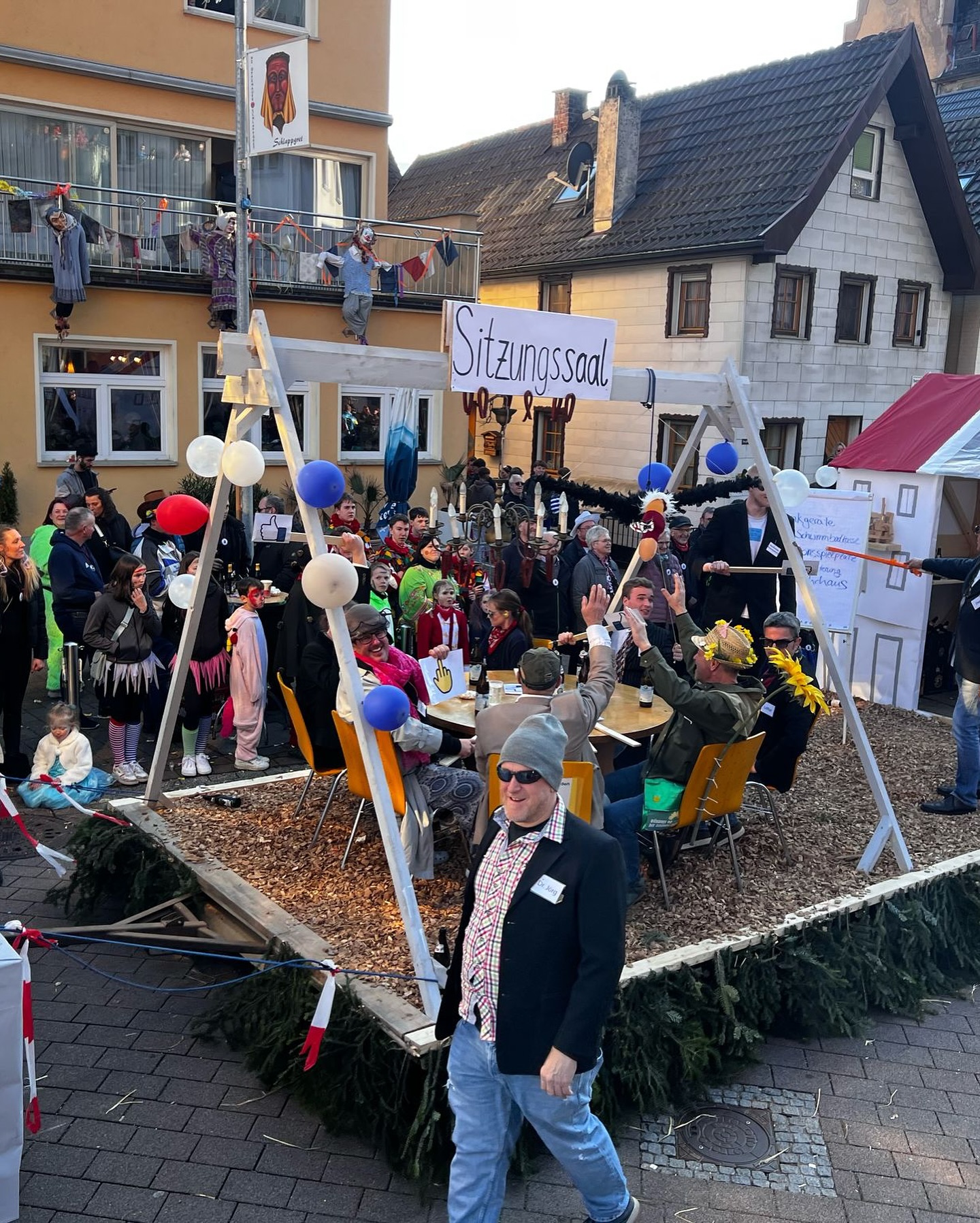 Eine Gruppe verkleideter Menschen feiert auf einem Wagen mit der Aufschrift "Sitzungssaal", umgeben von Zuschauern.
