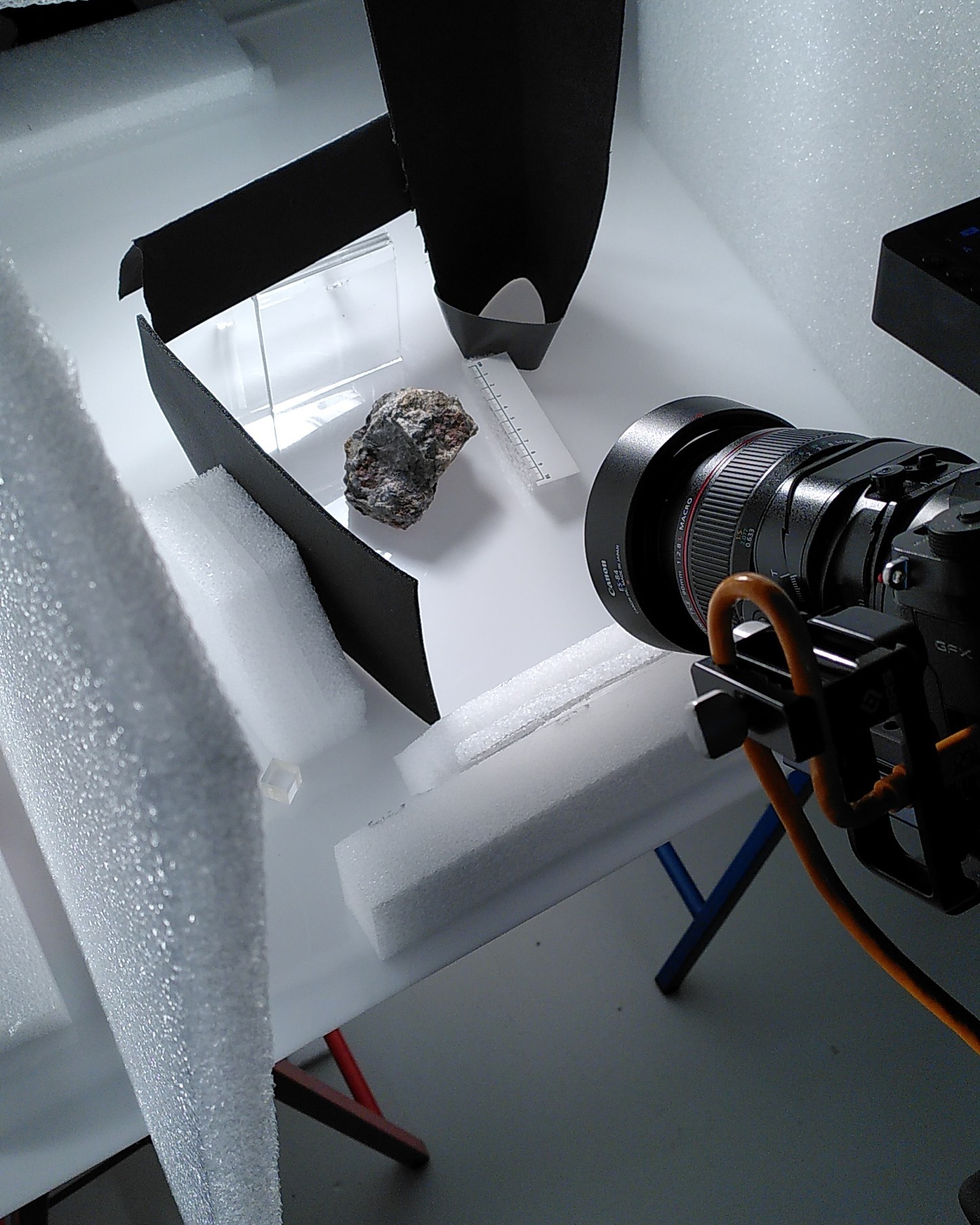 Dieser Alternativtext wurde KI-generiert: Ein Objekt liegt auf einer weißen Oberfläche, fotografiert mit einer Kamera. Umgebende Materialien sind weißes Schaumstoff und ein Teil eines Objektivs.