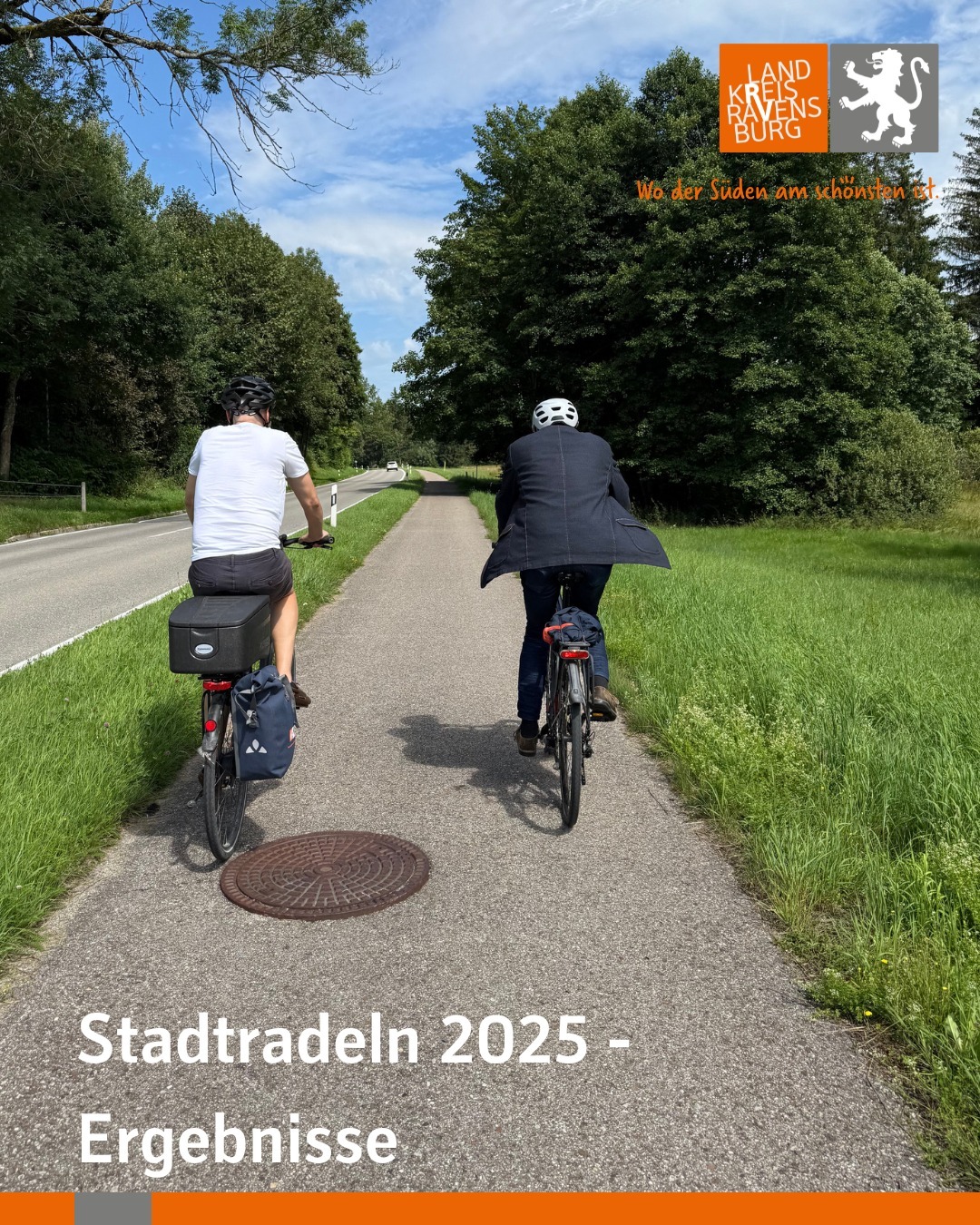 Zwei Personen fahren auf einem asphaltierten Weg nebeneinander Rad. Im Hintergrund befindet sich grüne Vegetation und ein Wolkenhimmel.