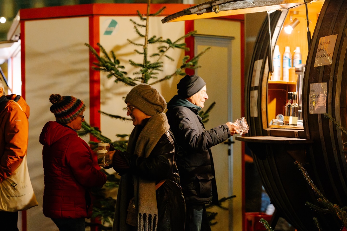 Personen kaufen an einem Weihnachtsmarkt Glühwein. Der Stand ist aus einem großen Weinfass gefertigt.