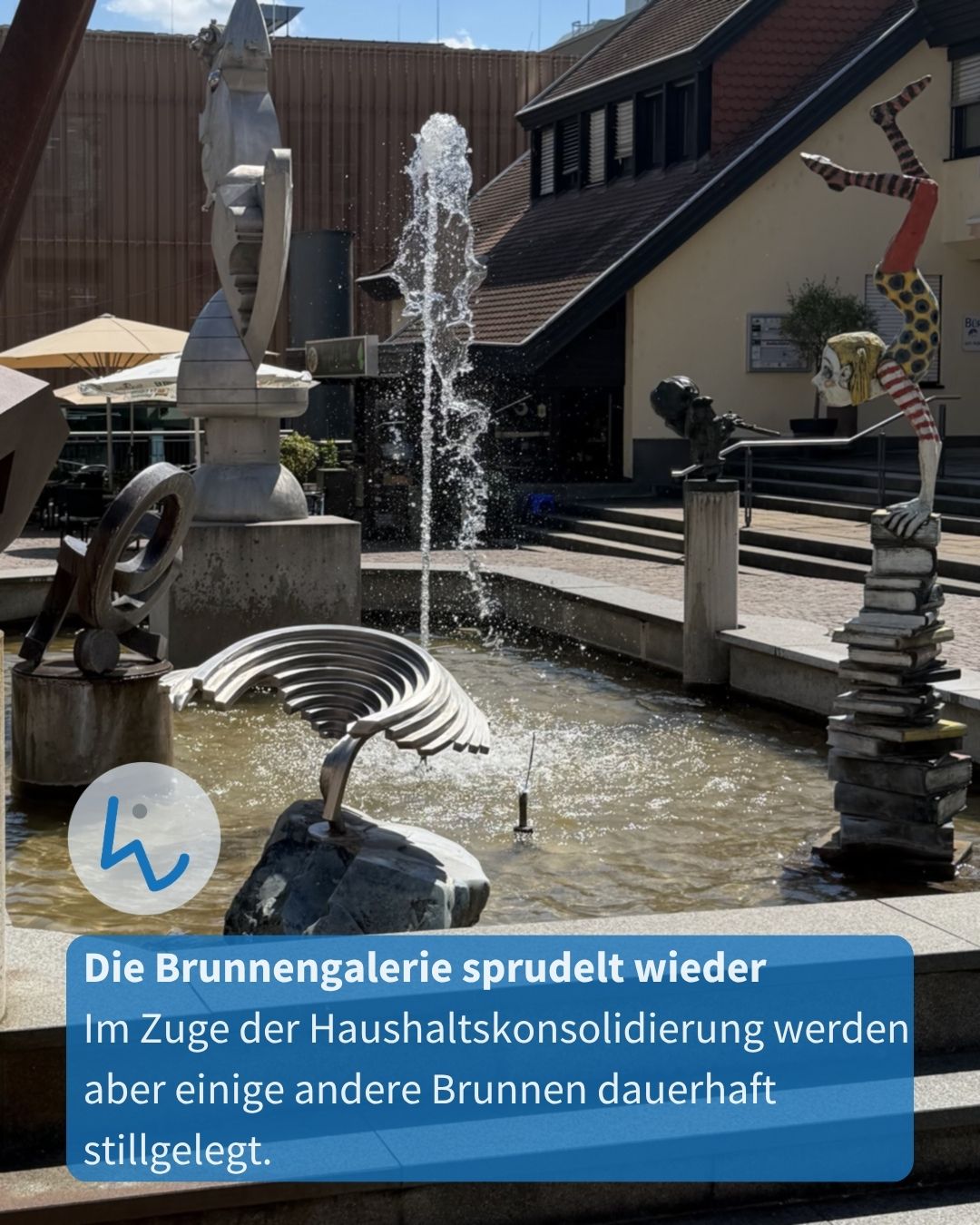 Ein Brunnen mit mehreren Skulpturen, darunter eine bunte Figur, die auf einem Stapel Bücher Handstand macht. Ein blauer Textkasten am unteren Rand lautet: „Die Brunnergalerie sprudelt wieder. Im Zuge der Haushaltskonsolidierung werden aber einige andere Brunnen dauerhaft stillgelegt.“ (KI-Alternativtext)