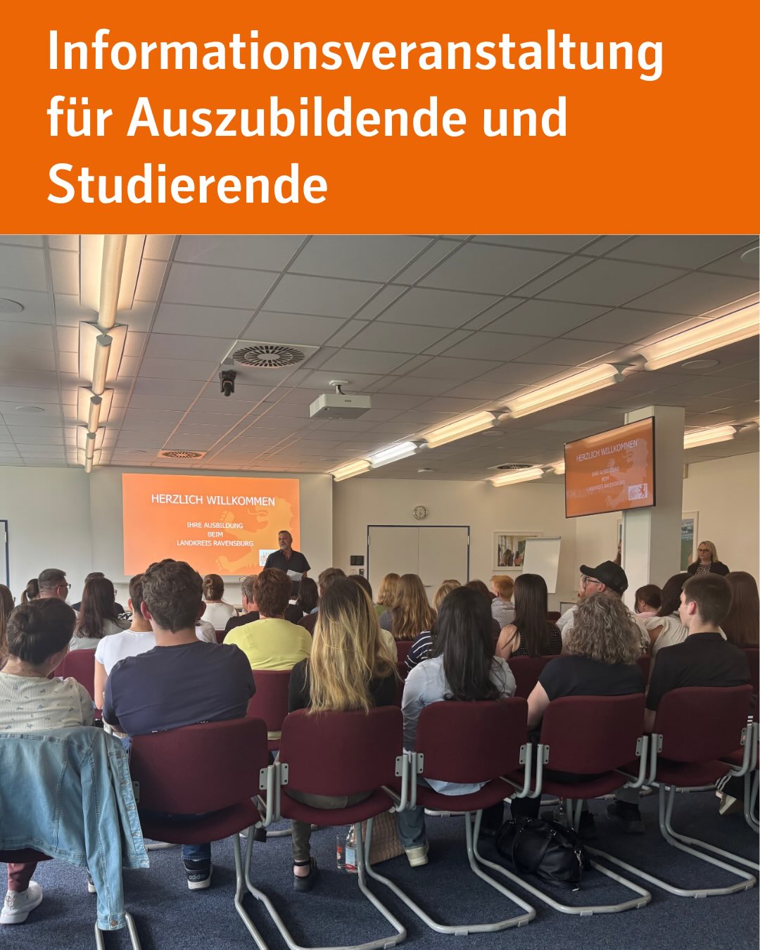 Informationsveranstaltung für Auszubildende und Studierende: Eine Person steht vor einem Publikum und spricht, hinter ihr ein Bildschirm mit der Aufschrift „Herzlich Willkommen – Ihre Ausbildung beim Landkreis Ravensburg“. (KI-Alternativtext)