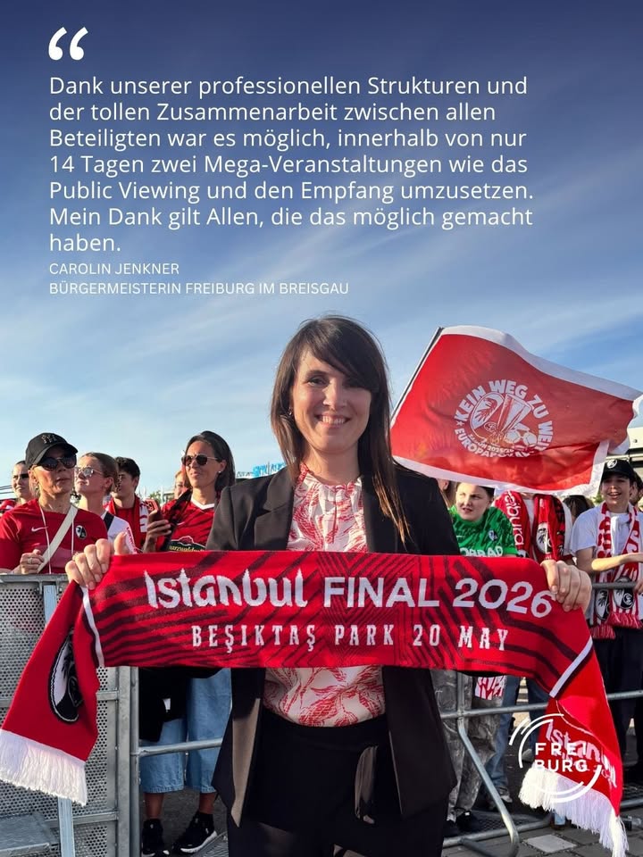 Eine Person hält einen roten Schal mit der Aufschrift „Istanbul FINAL 2026, Beşiktaş Park 20 May“ und eine rote Fahne mit dem Logo „Kein Weg zu weit“. Im Hintergrund steht eine Gruppe von Menschen, über dem Bild ist ein Zitat von Carolin Jenkner, Bürgermeisterin Freiburg im Breisgau, zu sehen. (KI-Alternativtext)