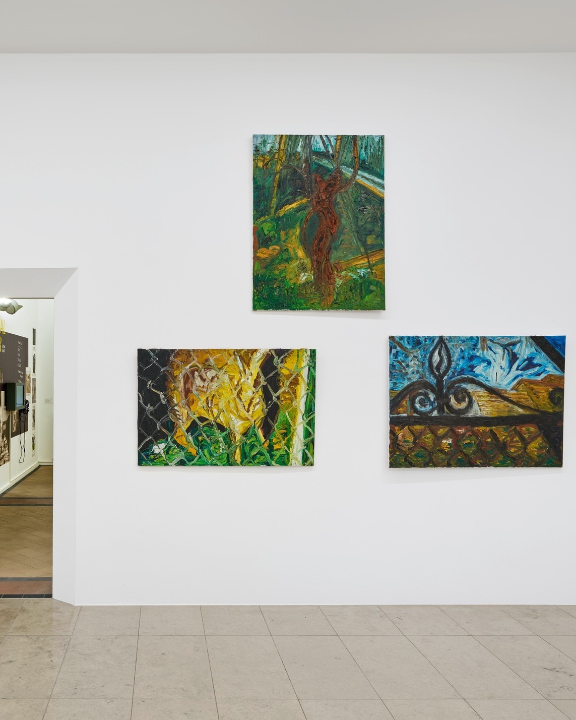 Dieser Alternativtext wurde KI-generiert: Ein Innenraum zeigt eine weiße Wand mit drei farbenfrohen Gemälden. Die Gemälde stellen abstrakte und naturalistische Motive dar.