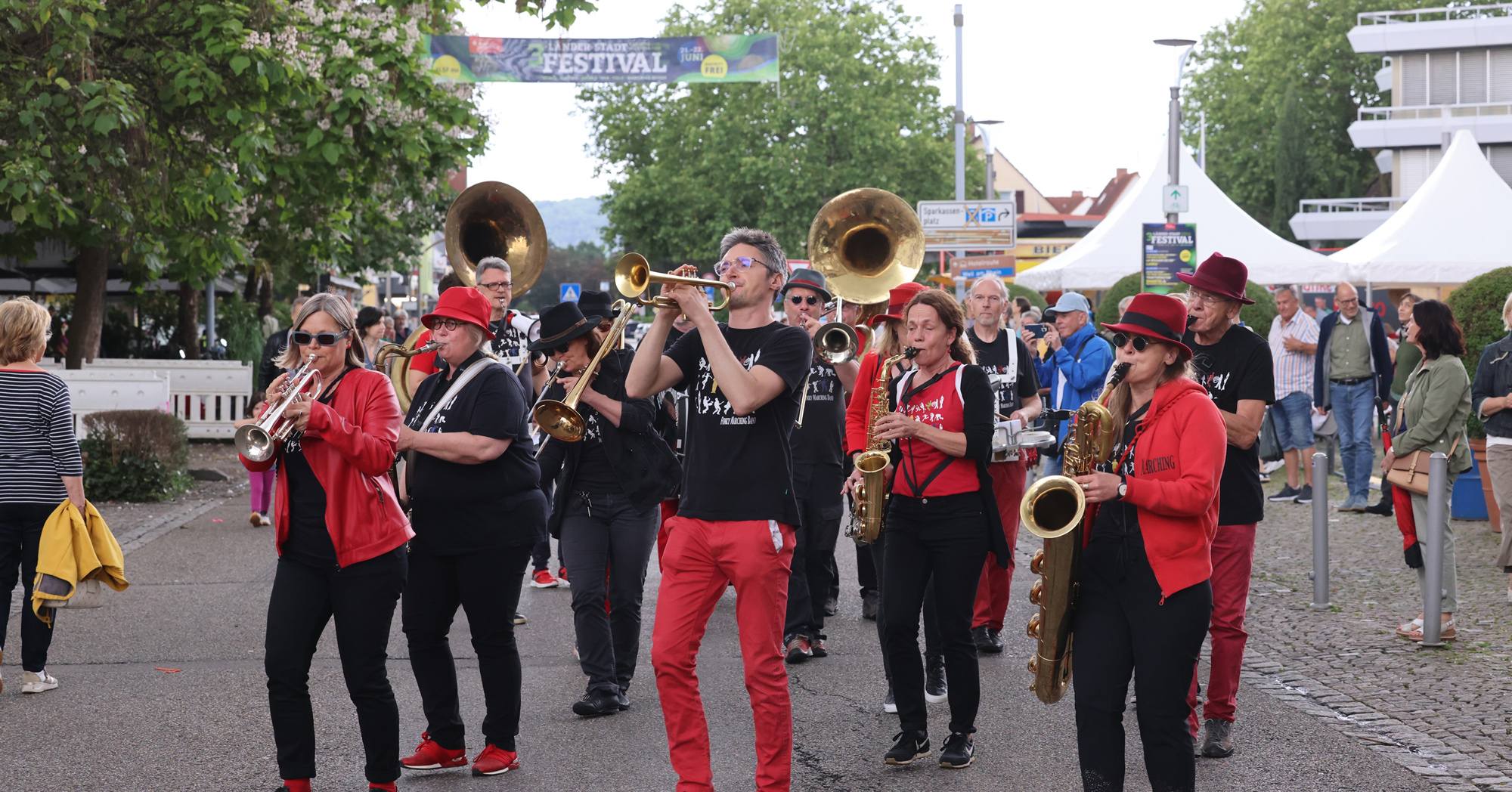 Eine Band spielt im Freien. Der Trompeter trägt eine rote Hose und ein schwarzes Shirt.
