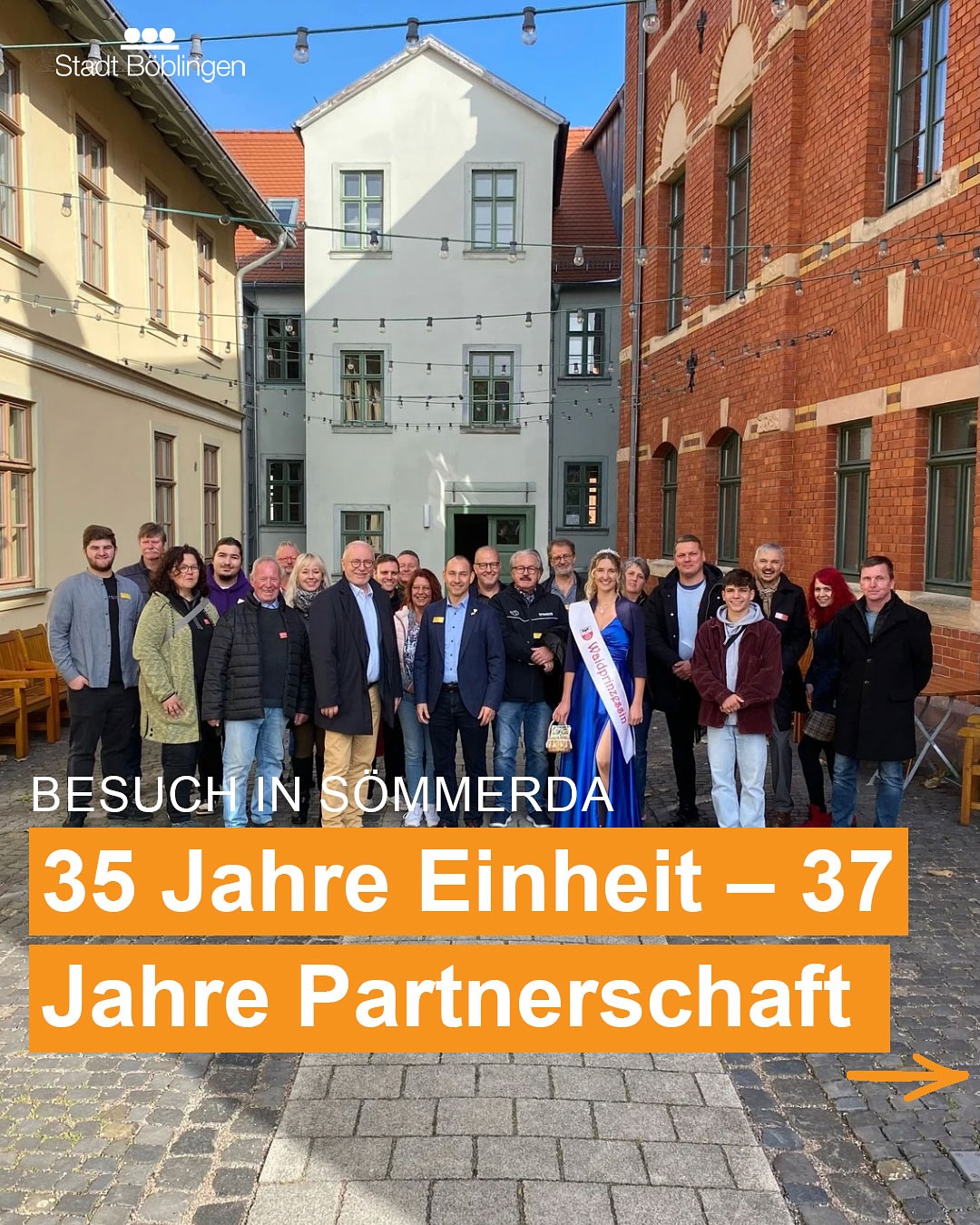 Dieser Alternativtext wurde KI-generiert: Eine Gruppe von Personen steht vor einem Gebäude mit einem verzierten Tor. Ein gelber Banner mit Text befindet sich im Vordergrund.