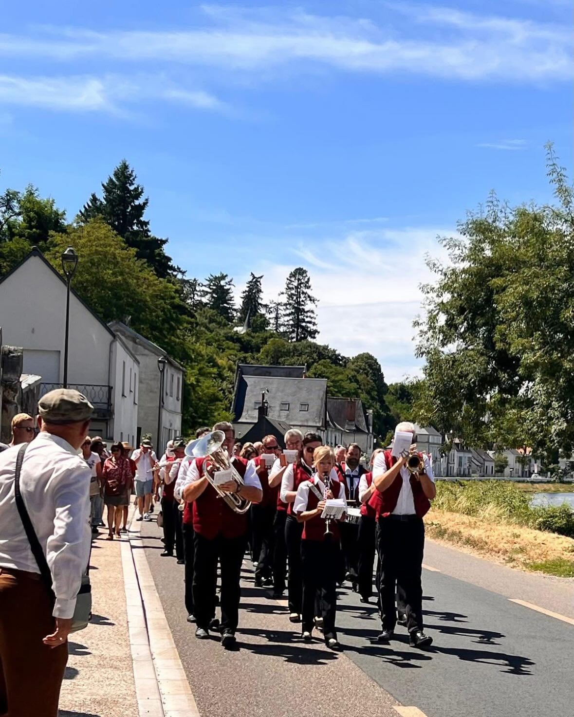 Eine Musikgruppe in passender Kleidung marschiert auf einer Straße. Im Hintergrund sind Gebäude und Bäume zu sehen.