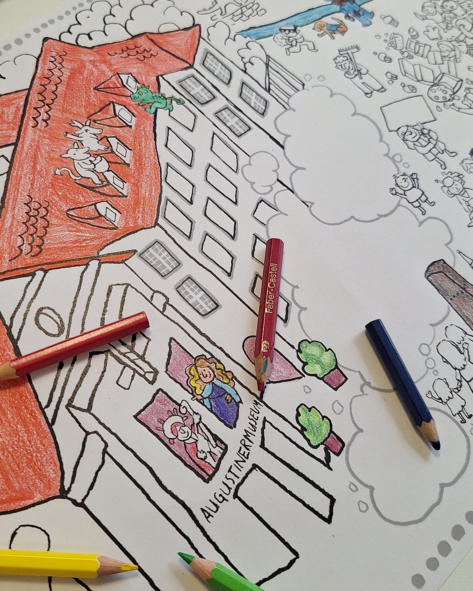 Dieser Alternativtext wurde KI-generiert: Schwarz-Weiß-Zeichnung einer Stadtansicht, teilweise farbig mit Buntstiften und angedeutetem Straßenverkehr. Mehrere Stifte liegen auf der Zeichnung.