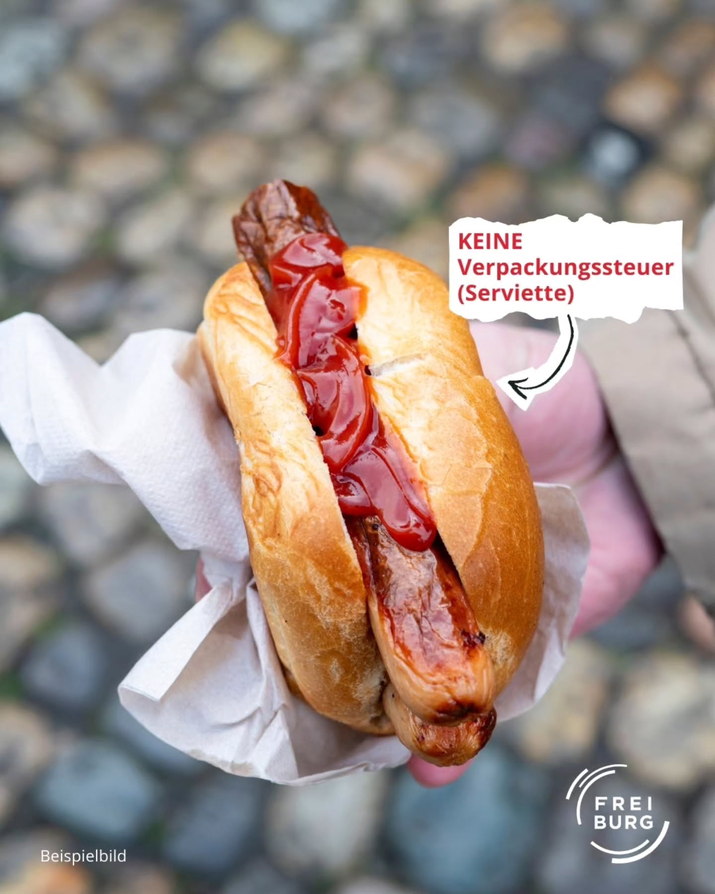Dieser Alternativtext wurde KI-generiert: Ein Würstchen mit Ketchup liegt in einer weißen Papiertüte. Auf dem Papier steht ein Text und ein Pfeil zeigt darauf.