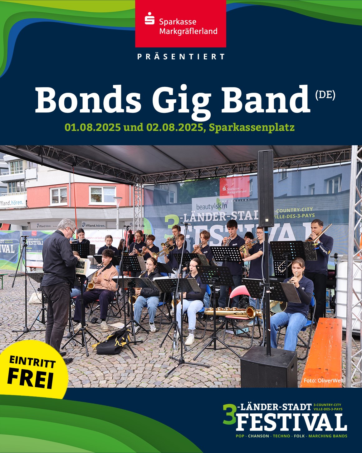 Eine Gruppe von Personen spielt auf der Bühne verschiedene Instrumente, wie Trompeten und Saxophone. Im Vordergrund steht der gelbe Schriftzug 'Eintritt frei'.