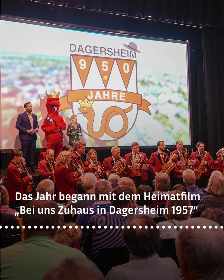 Dieser Alternativtext wurde KI-generiert: Ein großes Display zeigt eine Zahl und einen Wappen, vor dem Menschen mit Instrumenten und ein Maskottchen stehen. Im Vordergrund sind Menschen zu sehen, die möglicherweise ein Ereignis feiern.