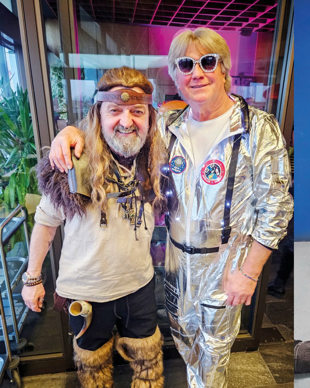 Dieser Alternativtext wurde KI-generiert: Zwei Personen in fantasievollen Kostümen posieren freundlich füreinander. Einer trägt ein Astronauten-Outfit, der andere ein Outfit im Stil eines Wikingers.