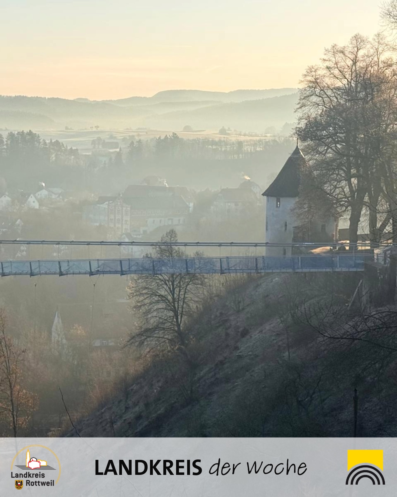 Dieser Alternativtext wurde KI-generiert: Eine Landschaftsaufnahme zeigt eine Stadt oder ein Dorf im Nebel. Eine Brücke führt über ein Tal, mit Gebäuden und Bäumen im Hintergrund.