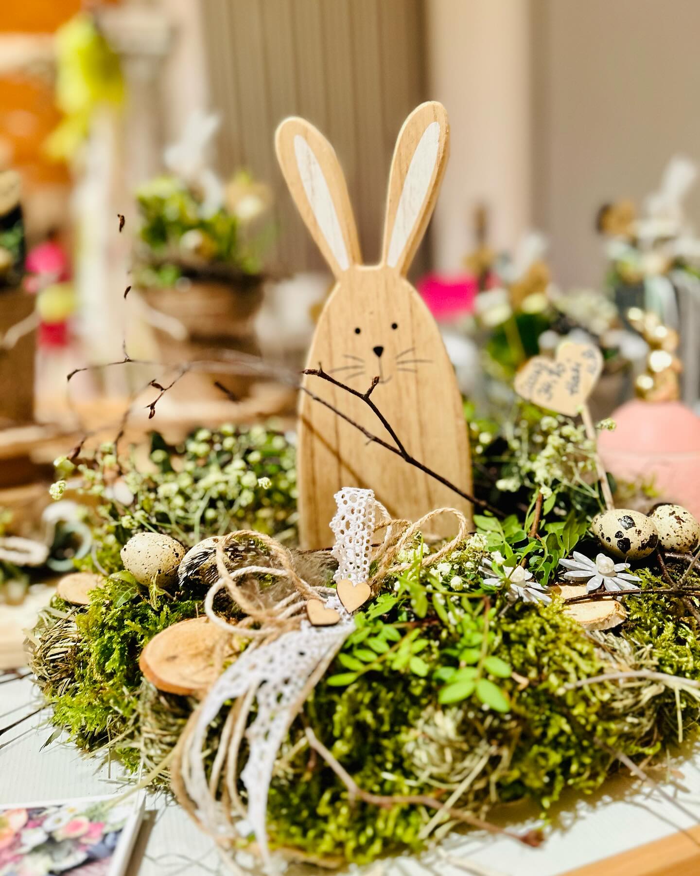 Nahaufnahme einer Feiertagsdekoration mit moosbedecktem Kranz, mit Eiern und einem Hasen aus Holz.