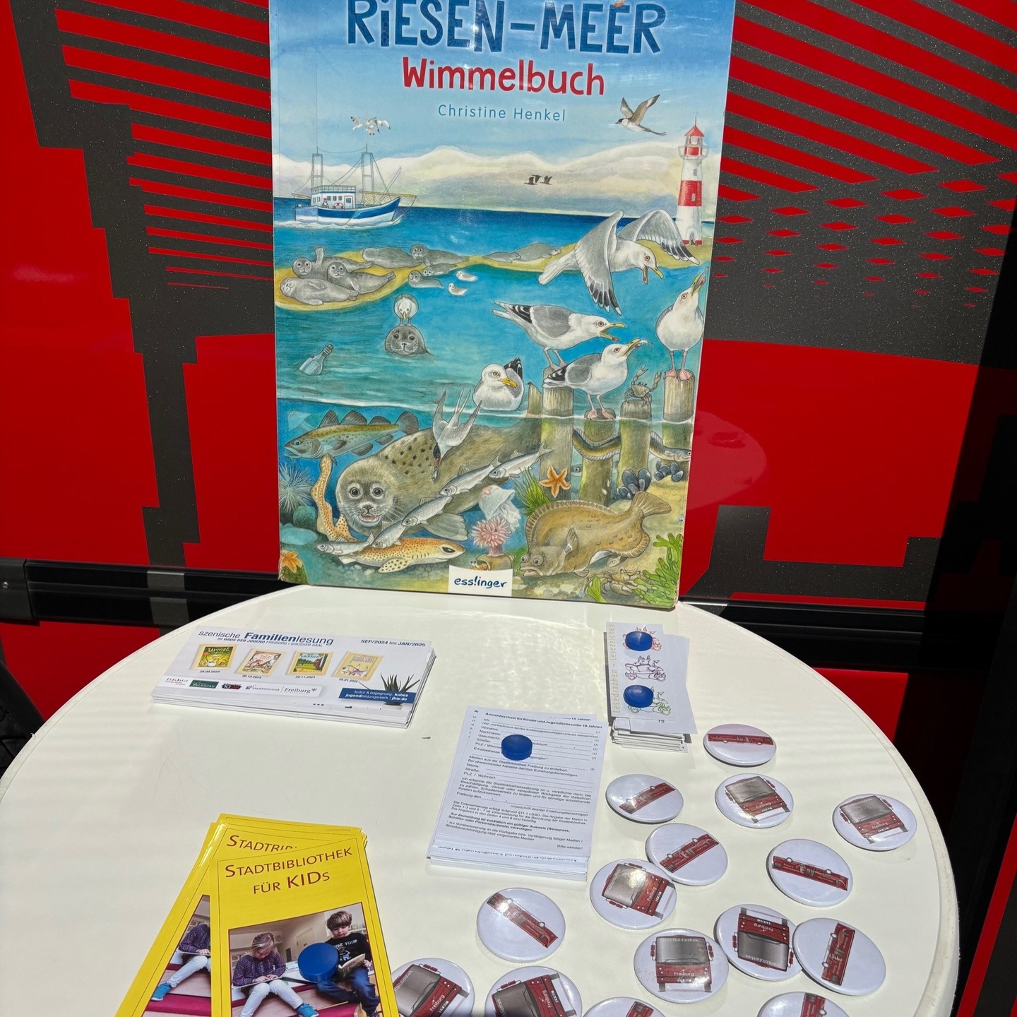 Ein Tisch mit Werbematerialien, darunter ein Wimmelbuch mit Meeresmotiven und verschiedene Anstecknadeln.