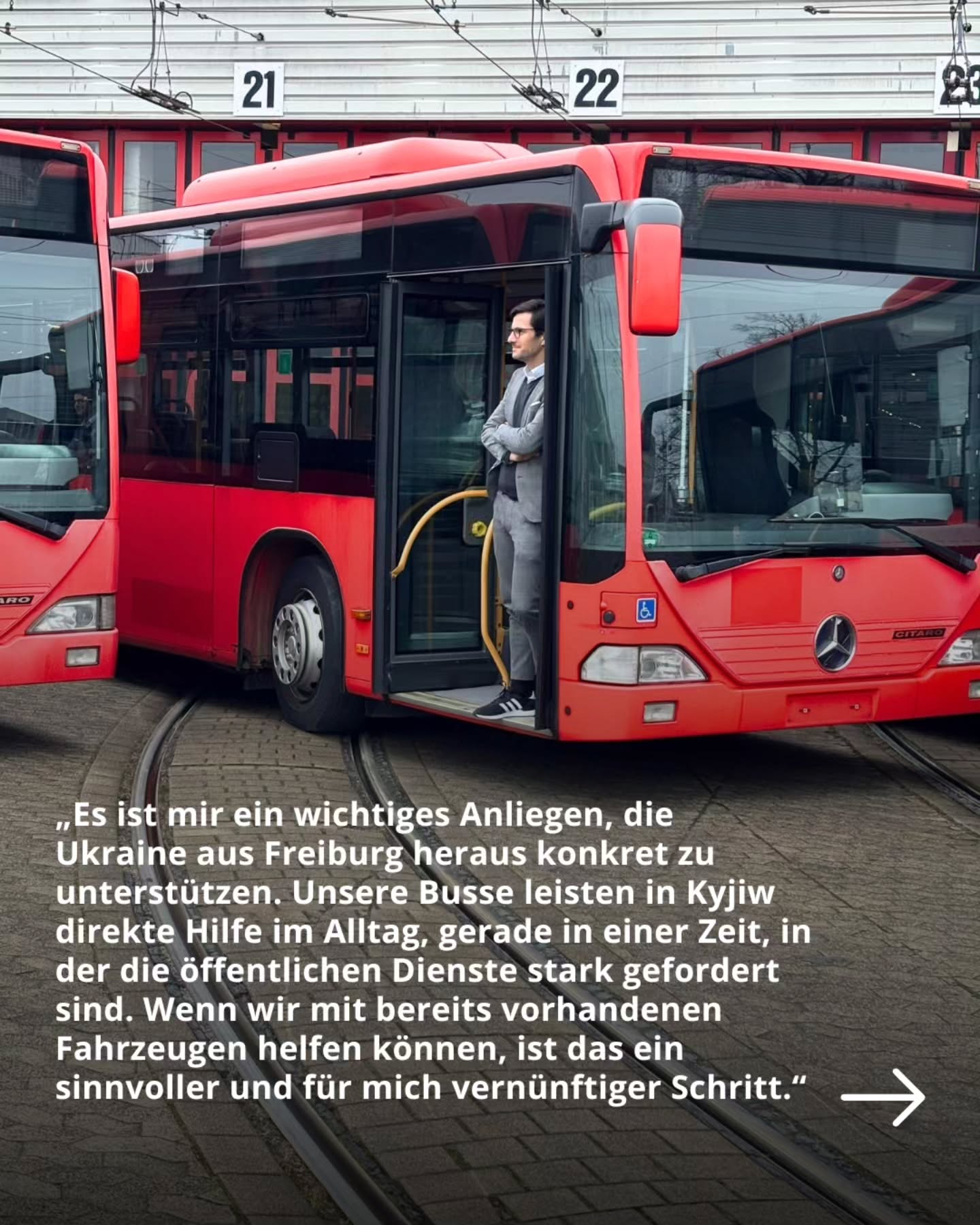 Dieser Alternativtext wurde KI-generiert: Ein Mann in einem Anzug steht vor roten Bussen mit den Nummern 21, 22 und 23. Im Bild ist ein Text zu sehen, der die Unterstützung der Ukraine thematisiert.