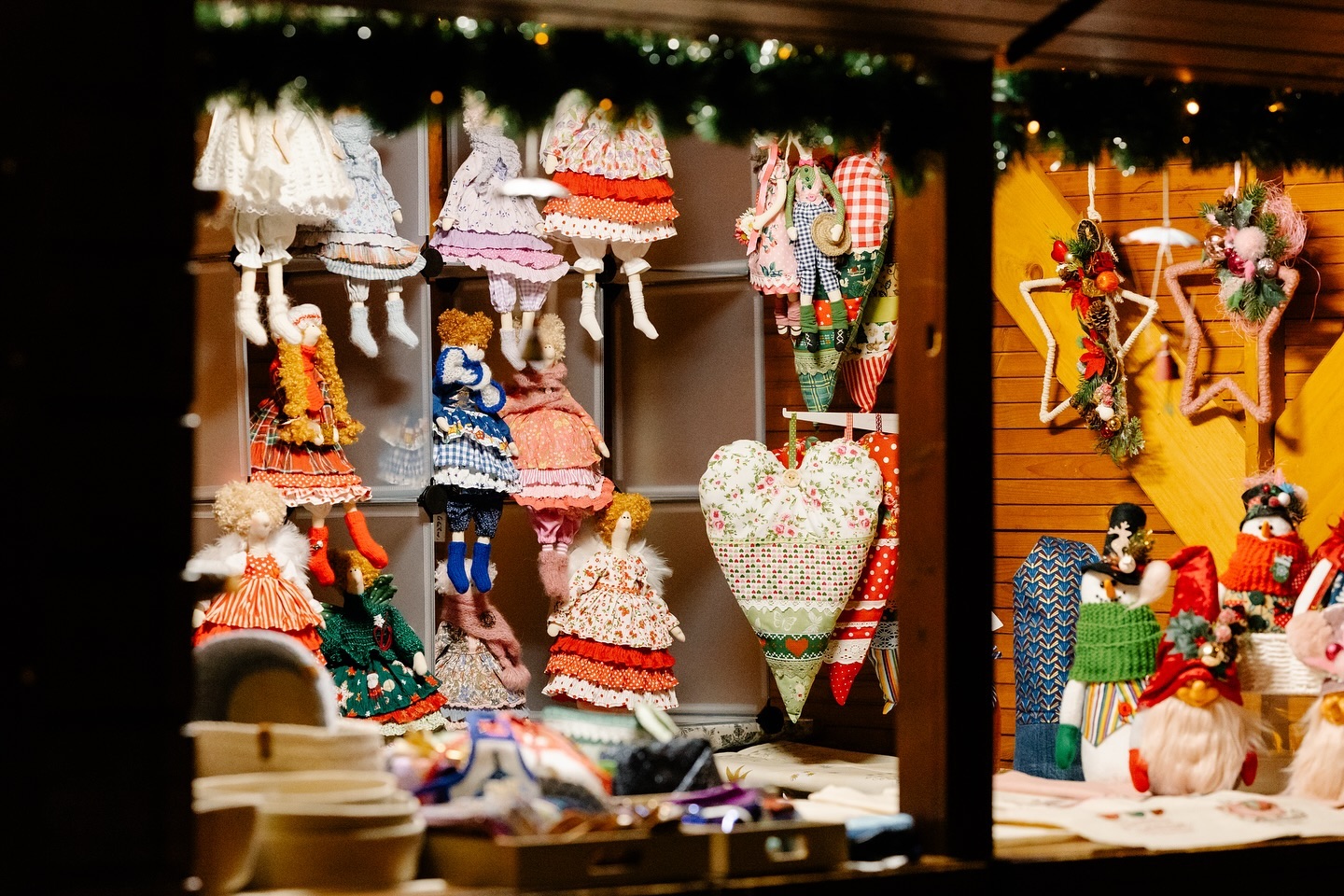 Handgefertigte Stoffpuppen und Weihnachtsdekoration sind in einem Verkaufsstand ausgestellt. Die Waren sind farbenfroh und detailliert gestaltet.