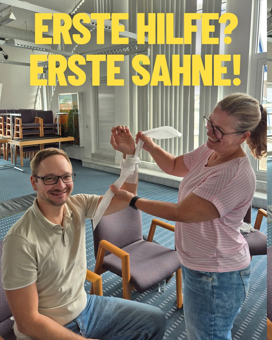 Zwei Personen demonstrieren eine Verbandtechnik, wobei eine sitzende Person den Arm hält und eine stehende Person einen weißen Verband um den Unterarm wickelt. Oben im Bild steht in großen gelben Buchstaben: „ERSTE HILFE? ERSTE SAHNE!“. (KI-Alternativtext)