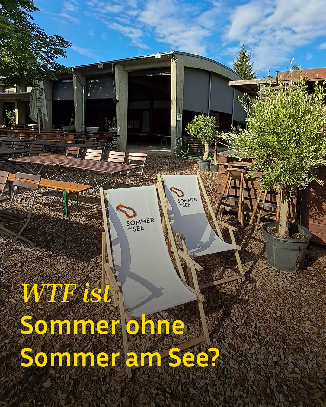 Zwei weiße Liegestühle mit dem Logo „Sommer am See“ stehen auf Holzspänen vor einem Gebäude mit Außenbereich und Tischen. Im unteren Bildbereich ist der gelbe Text „WTF ist Sommer ohne Sommer am See?“ eingeblendet. (KI-Alternativtext)