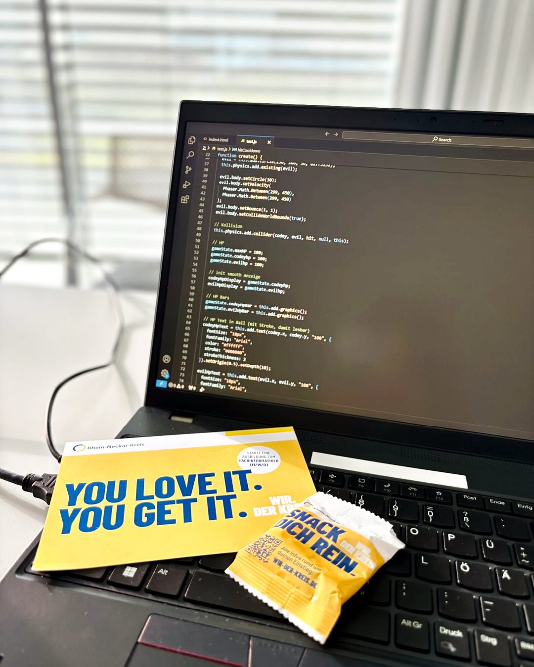 Dieser Alternativtext wurde KI-generiert: Ein Laptop steht auf einem Schreibtisch mit einer Tasse Kaffee, einem Notizblock und einem Snack. Auf dem Bildschirm ist Code zu sehen.