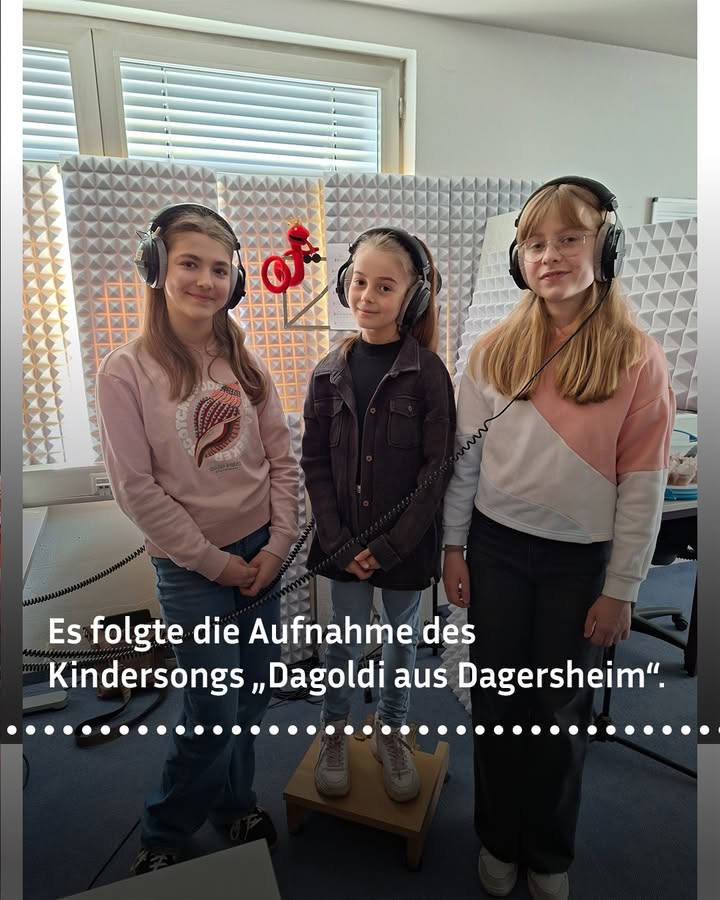 Dieser Alternativtext wurde KI-generiert: Zwei Personen mit Kopfhörern sitzen vor einer schallgedämmten Wand. Ein rotes Objekt ist zwischen ihnen platziert.