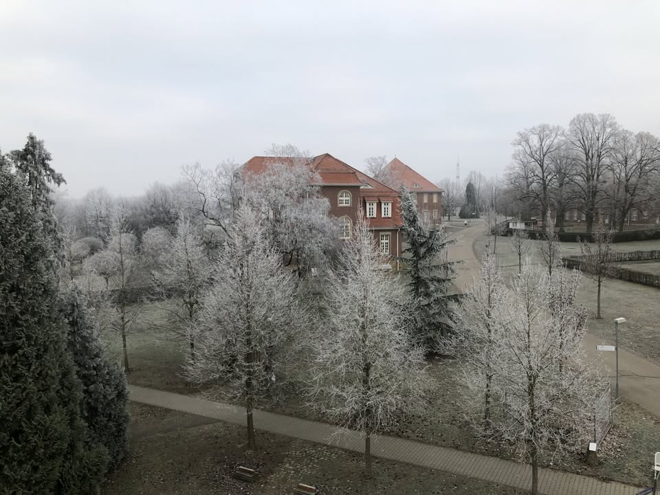 Dieser Alternativtext wurde KI-generiert: Ein Gebäude mit einem roten Dach ist von Bäumen mit Reif bedeckt. Das Schwarz-Weiß-Bild zeigt eine winterliche Landschaft.