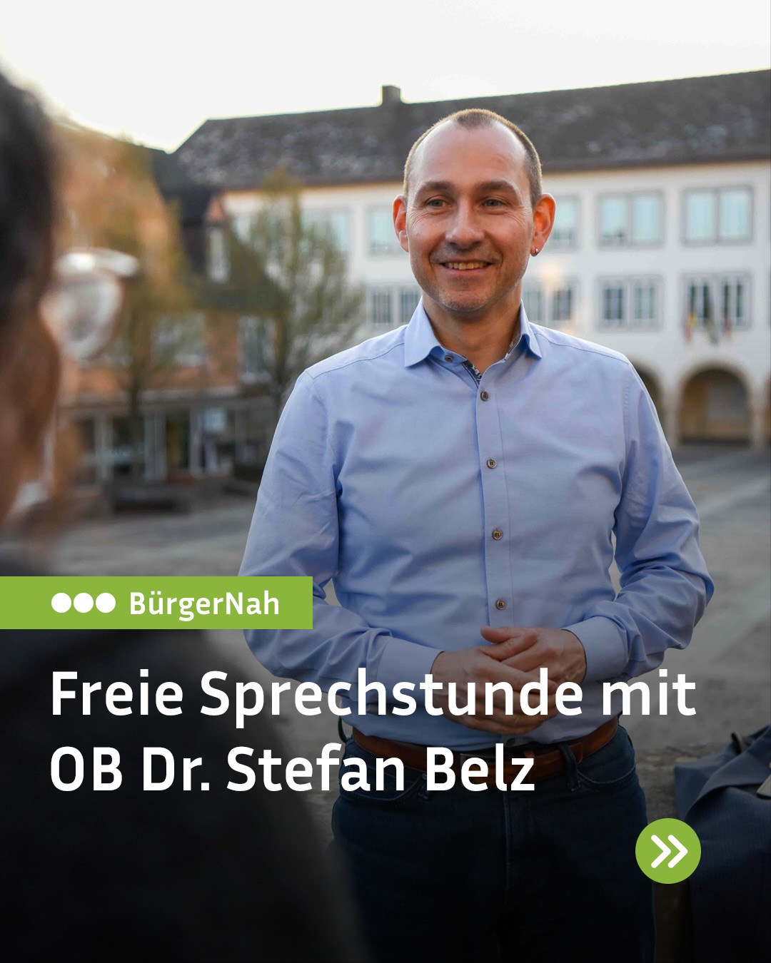Dieser Alternativtext wurde KI-generiert: Ein lächelnder Mann steht im Freien vor einem Gebäude. Im Vordergrund befindet sich Text und ein Logo.