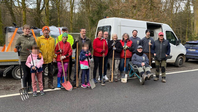 Dieser Alternativtext wurde KI-generiert: Eine Gruppe von Menschen steht lächelnd im Freien vor einem weißen Transporter und einem Anhänger. Sie halten Werkzeuge wie Spaten und Rechen.