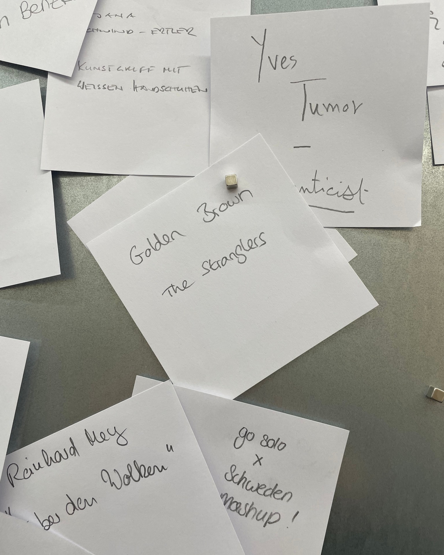 Dieser Alternativtext wurde KI-generiert: Mehrere Notizzettel mit handschriftlichem Text liegen überlappend auf einer grauen Fläche. Der Hintergrund ist unscharf und die Notizen scheinen an einer Wand befestigt zu sein.
