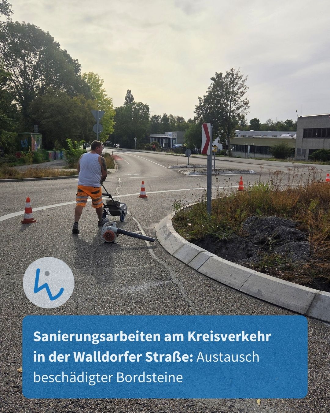 Eine Person reinigt die Fahrbahn mit einem Bläser, umgeben von Verkehrskegel. Ein blauer Textkasten unten lautet: Sanierungsarbeiten am Kreisverkehr in der Walldorfer Straße: Austausch beschädigter Bordsteine. (KI-Alternativtext)