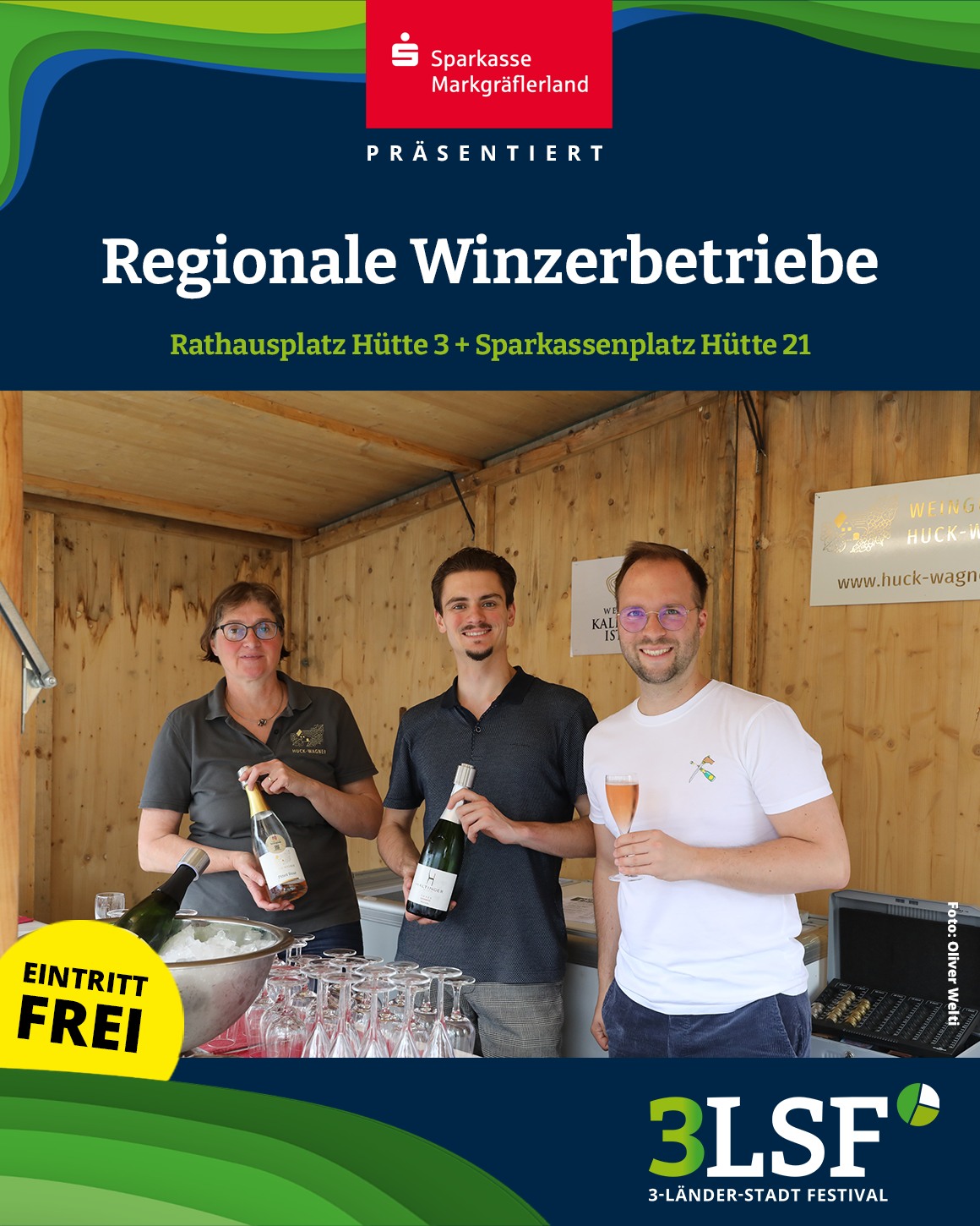 Dieser Alternativtext wurde KI-generiert: Eine Gruppe von Personen steht unter einem Zeltdach vor einer Weinhandlung. Sie halten Gläser und Flaschen mit Getränken in der Hand.