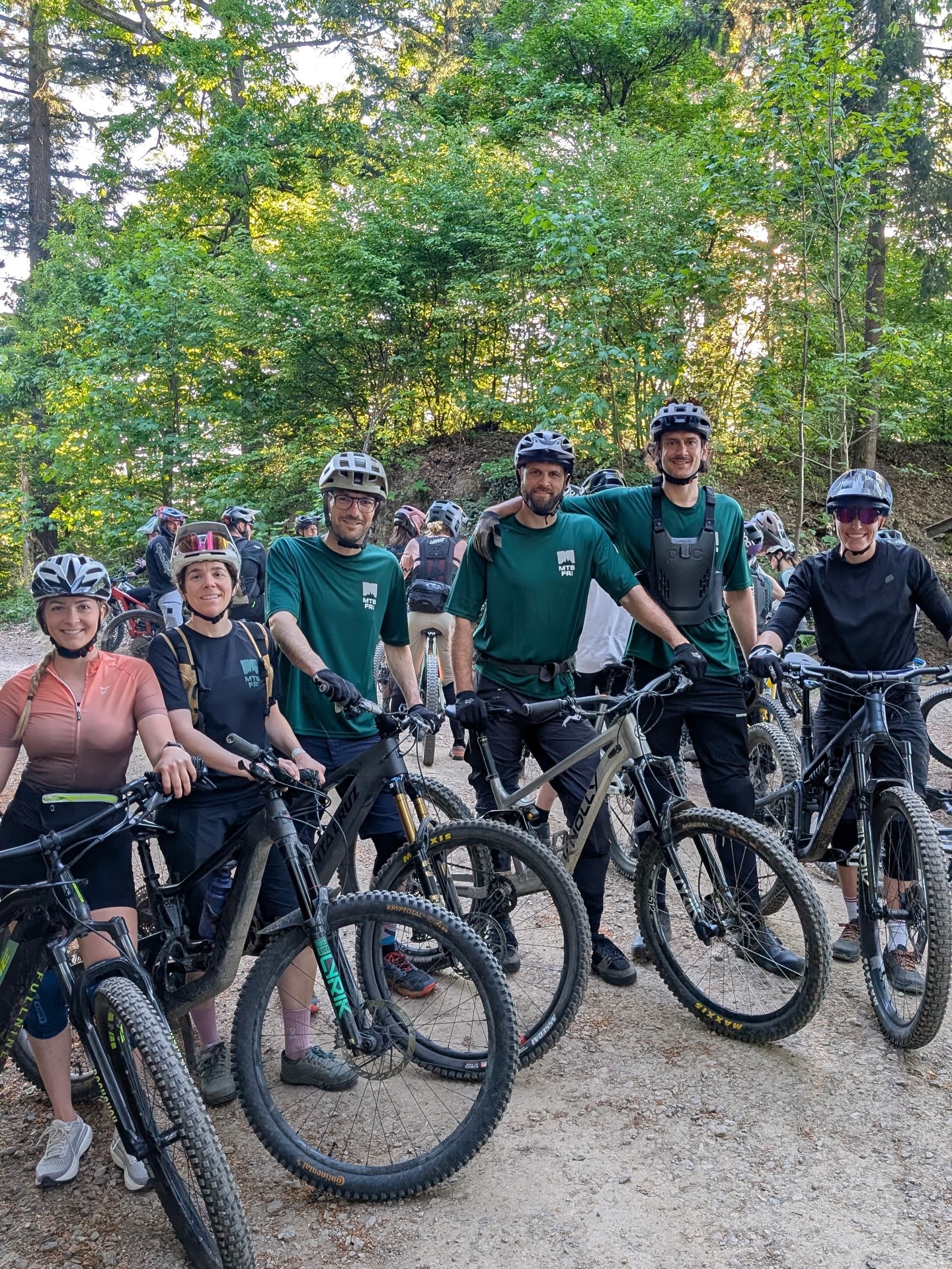 Dieser Alternativtext wurde KI-generiert: Eine Gruppe von Menschen steht mit Fahrrädern in einem Wald. Sie tragen sportliche Kleidung und lächeln in die Kamera.