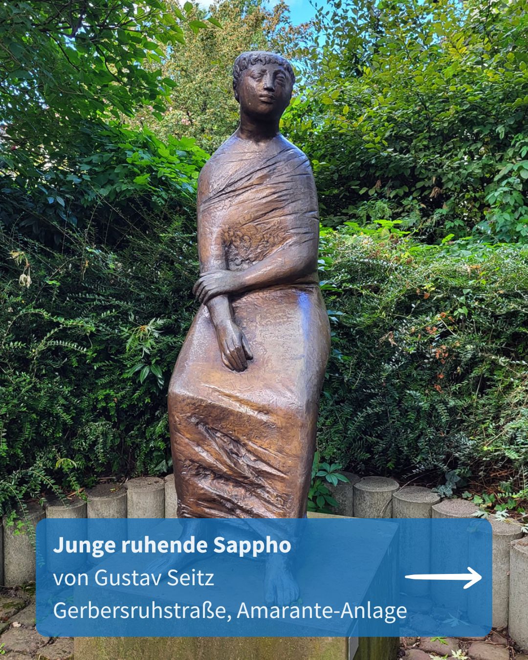 Bronzene Skulptur einer sitzenden, in Stoff gehüllten Figur mit geschlossenen Augen, umgeben von Grünanlagen. Unten Text: „Junge ruhende Sappho von Gustav Seitz, Gerbersruhstraße, Amarante-Anlage“. (KI-Alternativtext)