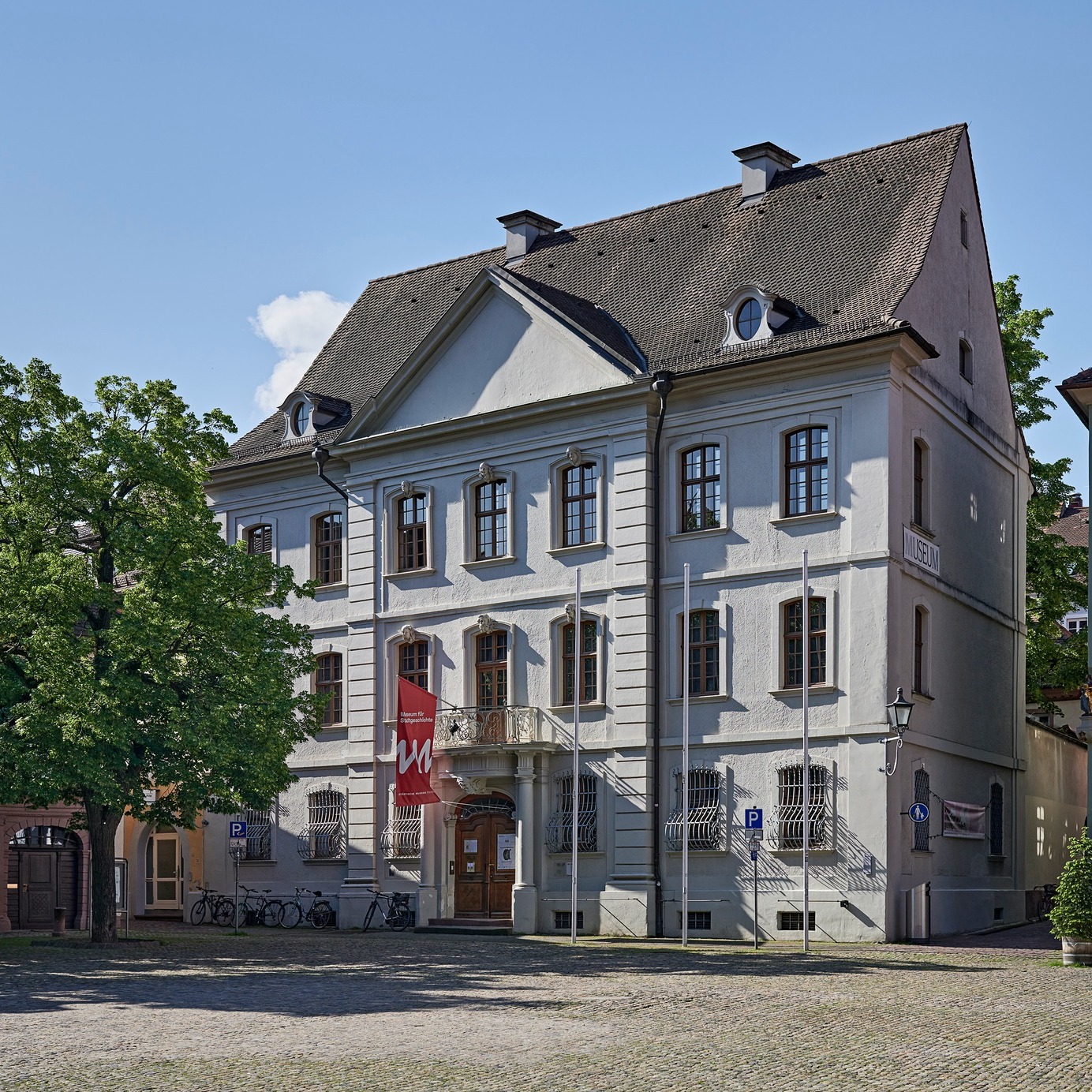  Das abgebildete Gebäude ist ein dreistöckiges, barockes Gebäude mit einem Mansarddach. Es hat eine symmetrische Fassade mit je drei Fenstern pro Stockwerk. In der Mitte des Gebäudes befindet sich ein Eingang mit einer Freitreppe.
