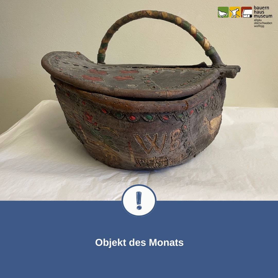 Alter, verzierter Korb mit Deckel und Henkel, bemalt mit Mustern und den Buchstaben „WB“, präsentiert als „Objekt des Monats“ vom Bauernhausmuseum. (KI-Alternativtext)