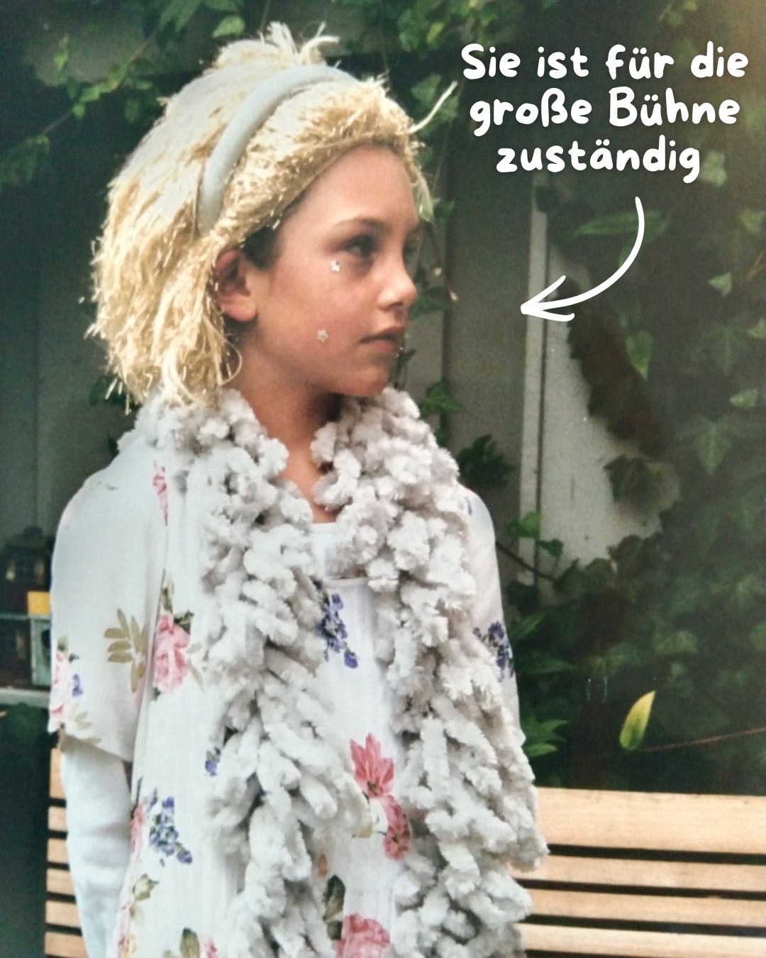 Dieser Alternativtext wurde KI-generiert: Eine Person mit blonden Haaren und einem Blumenschmuck trägt ein geblümtes Oberteil. Das Bild ist in Farbe und zeigt eine Nahaufnahme der Person.