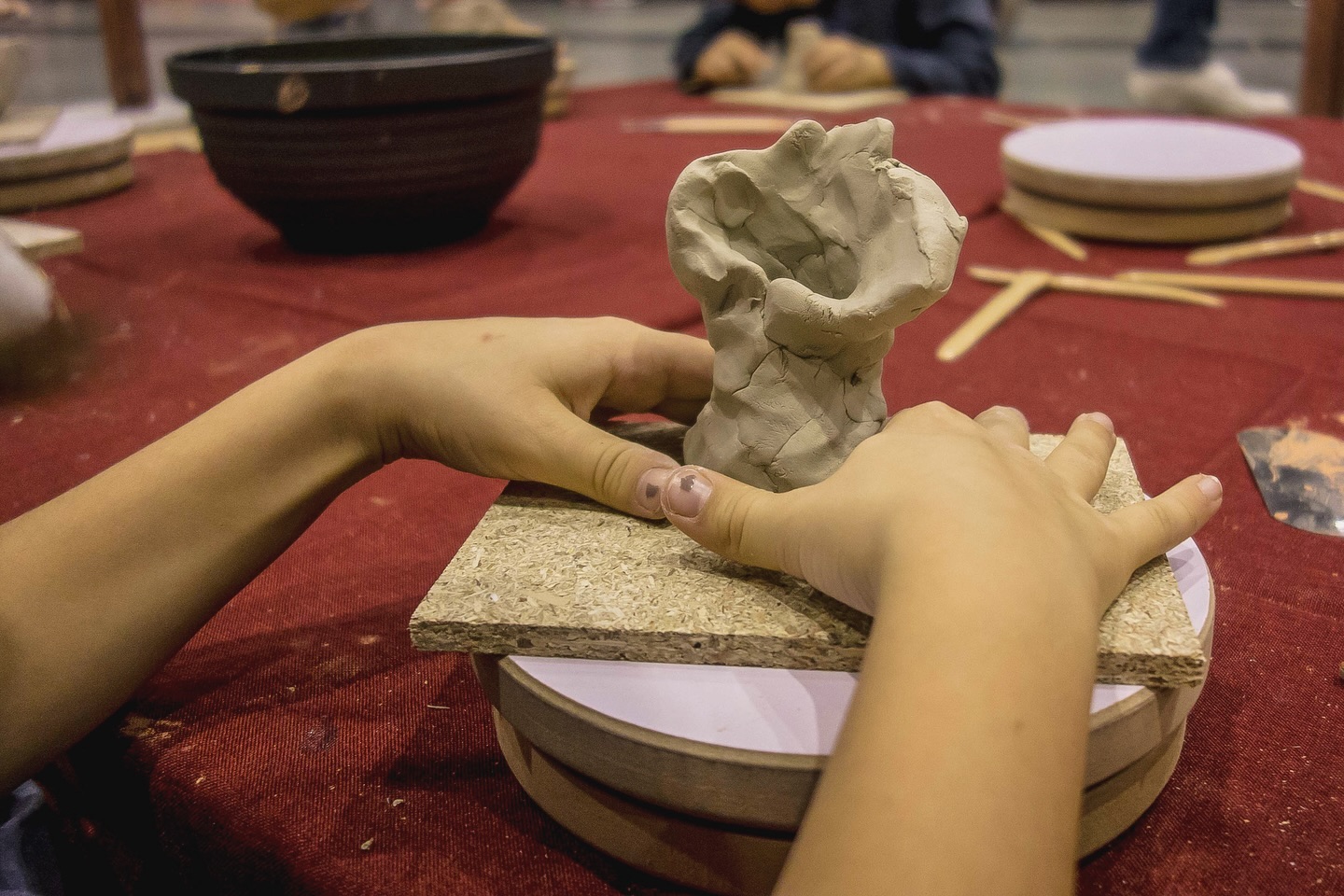Ein Kind formt einen Tonklumpen auf einer Drehscheibe. Die Hände des Kindes sind deutlich zu sehen.