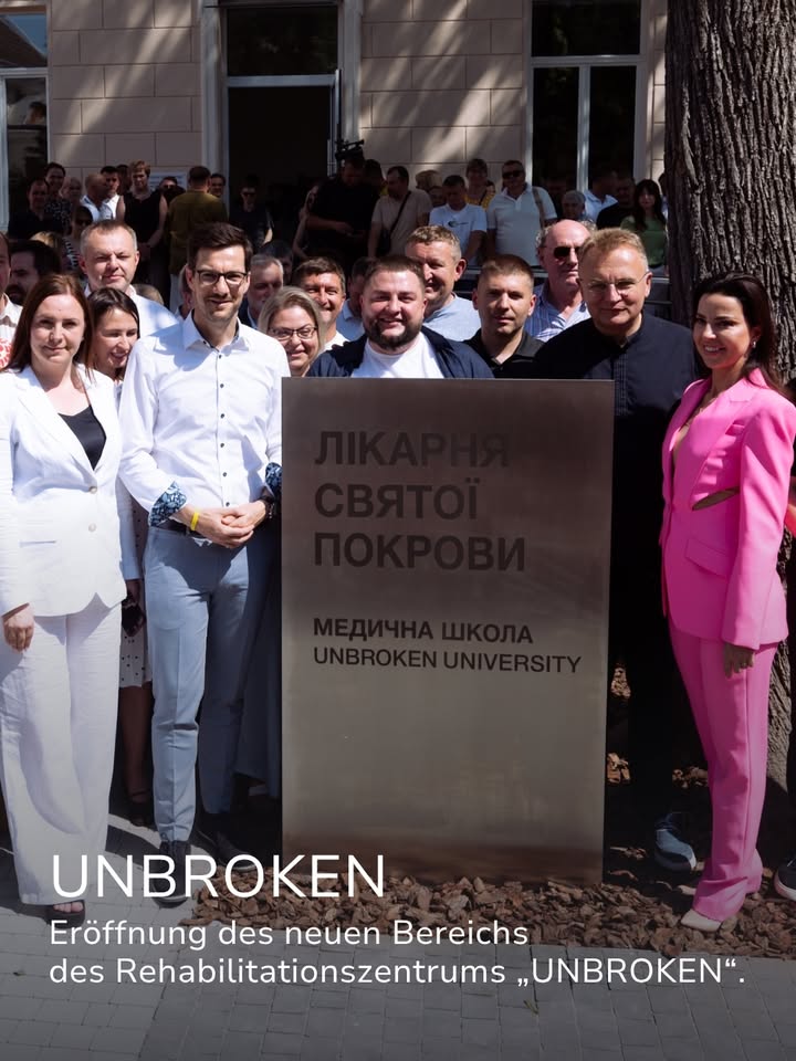 Eine Gruppe von Personen steht vor einer großen Metalltafel mit der Aufschrift „ЛІКАРНЯ СВЯТОЇ ПОКРОВИ“ und „МЕДИЧНА ШКОЛА UNBROKEN UNIVERSITY“. Ein Textoverlay unten gibt an, dass es sich um die Eröffnung des neuen Bereichs des Rehabilitationszentrums „UNBROKEN“ handelt. (KI-Alternativtext)