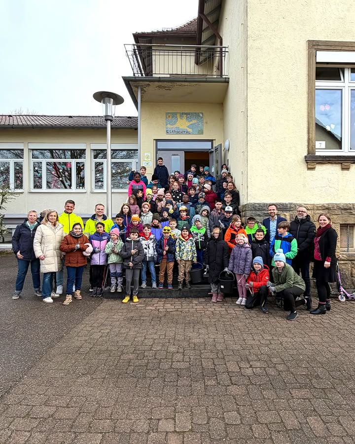 Dieser Alternativtext wurde KI-generiert: Eine große Gruppe von Menschen steht vor einem Gebäude mit Fenstern und einem Eingang. Das Bild ist farbig und zeigt eine Außenaufnahme.